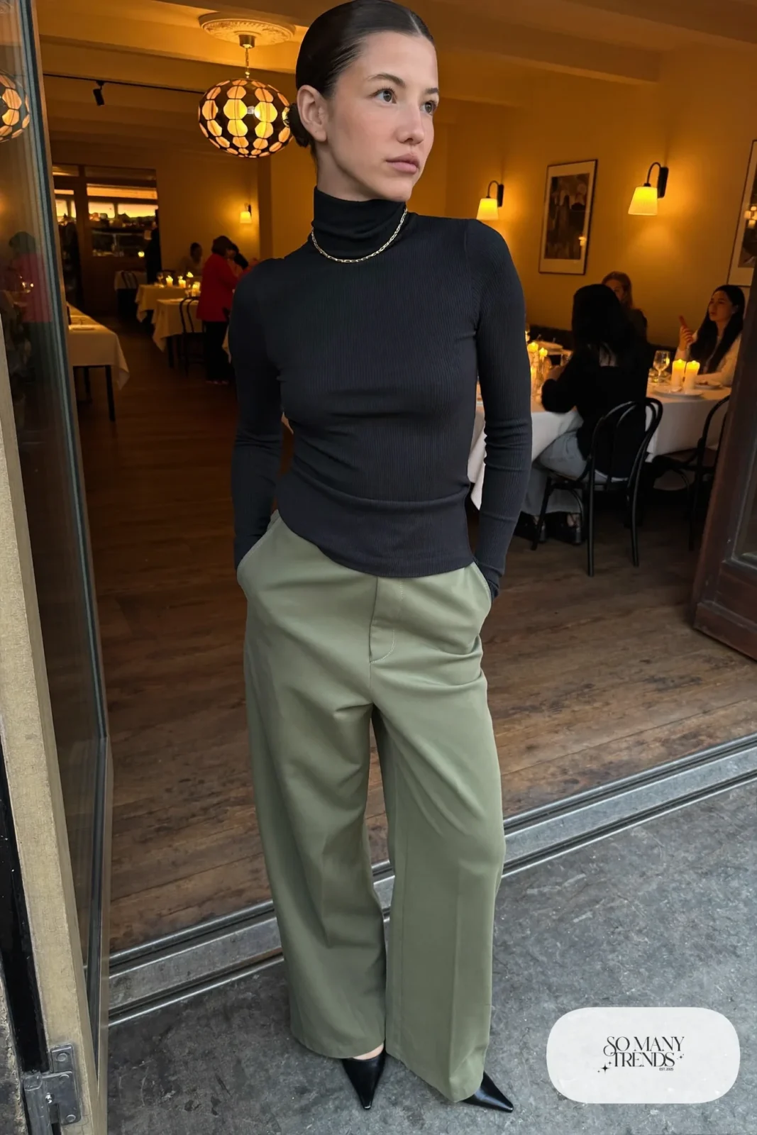 Woman in a black fitted turtleneck, olive wide-leg pants and black pointed pumps, outfit 19