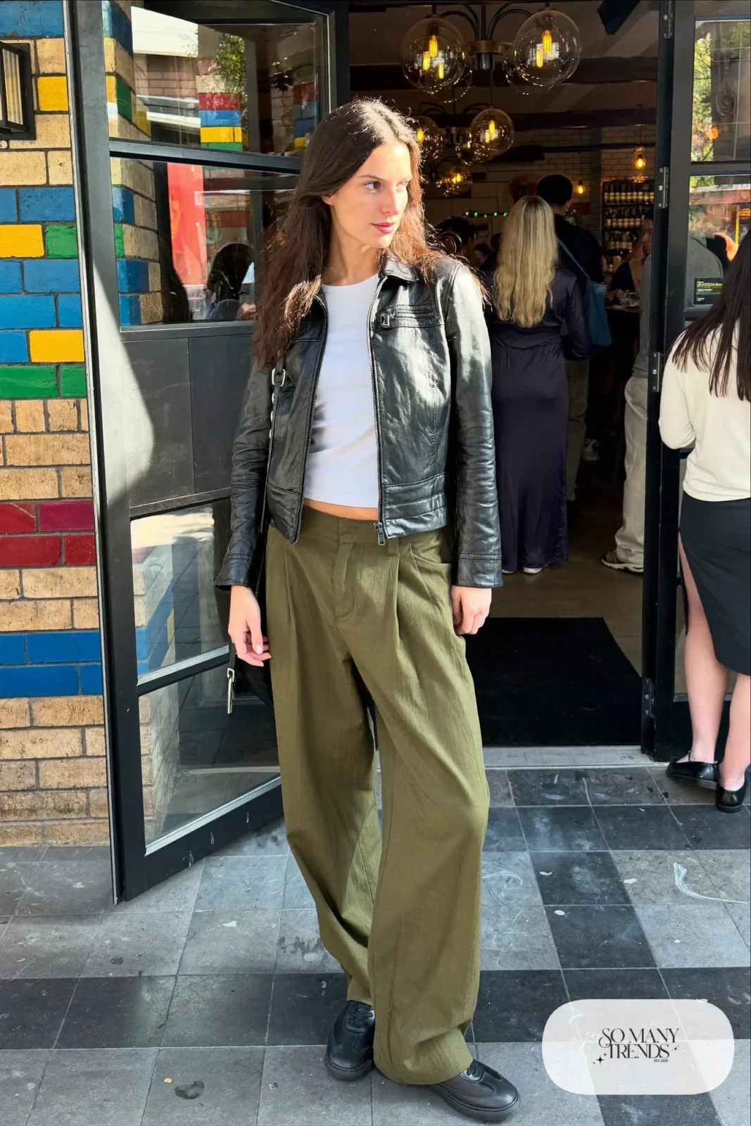 Woman in a short black leather jacket, white tee, olive wide-leg pants and black boots-free sneakers, outfit 22