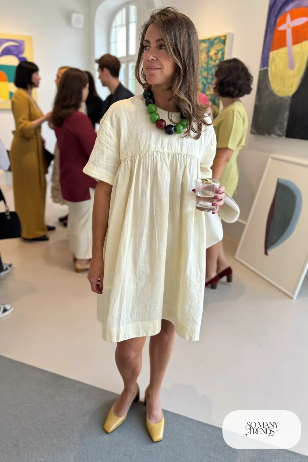 Woman in a cream shift dress with oversized wooden and colored beads necklace and tan block heels, outfit 3