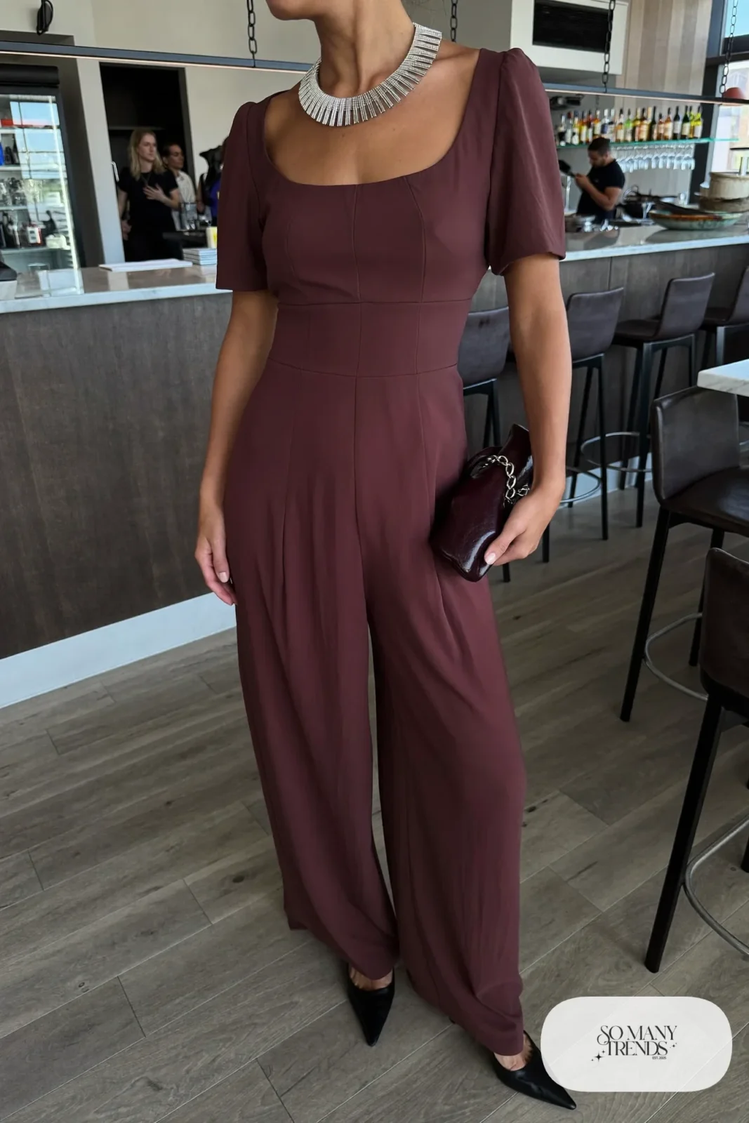 Woman in a wine wide-leg jumpsuit with a bold silver collar necklace and black heels, outfit 8
