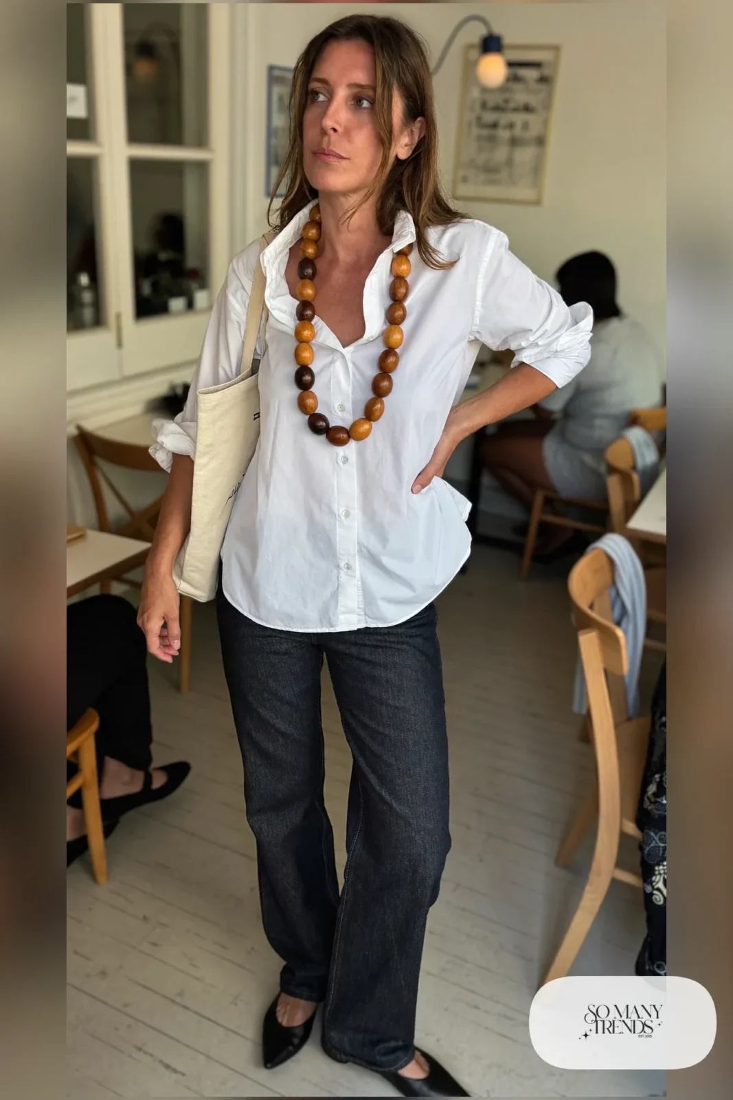 Woman in a white poplin shirt with open collar, dark straight jeans, large wooden beads and black flats, outfit 13