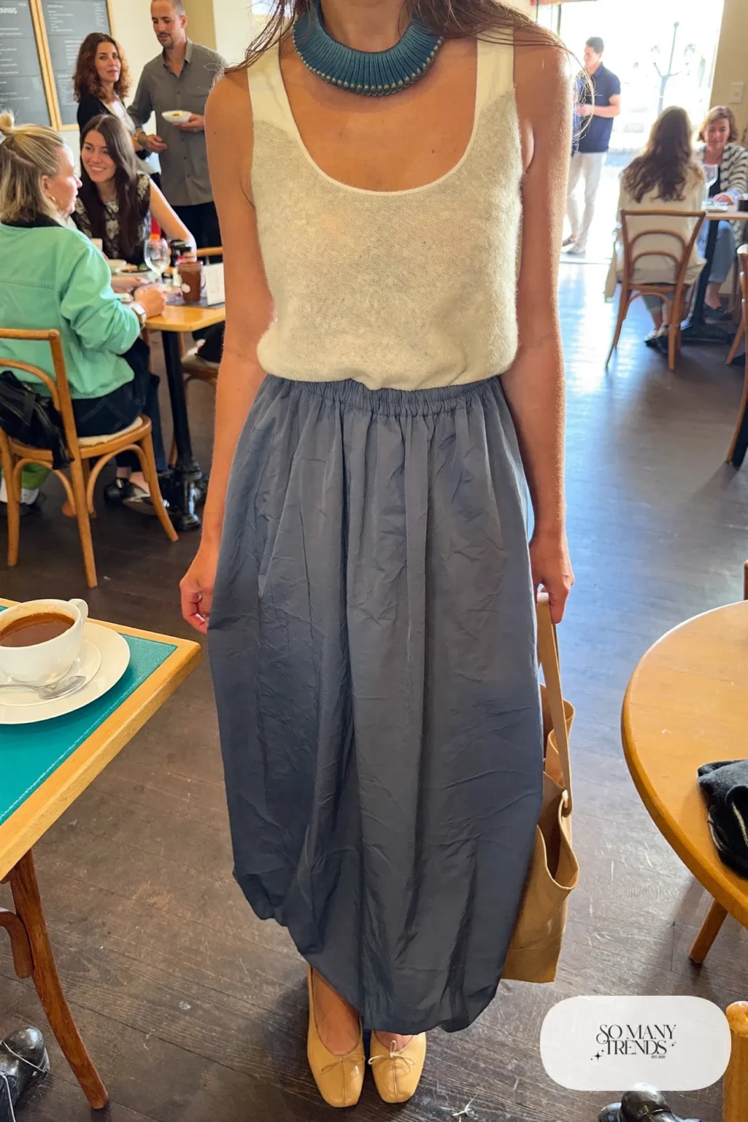 Woman in a cream knit vest, long slate blue skirt, bold resin necklace and tan flats, outfit 17