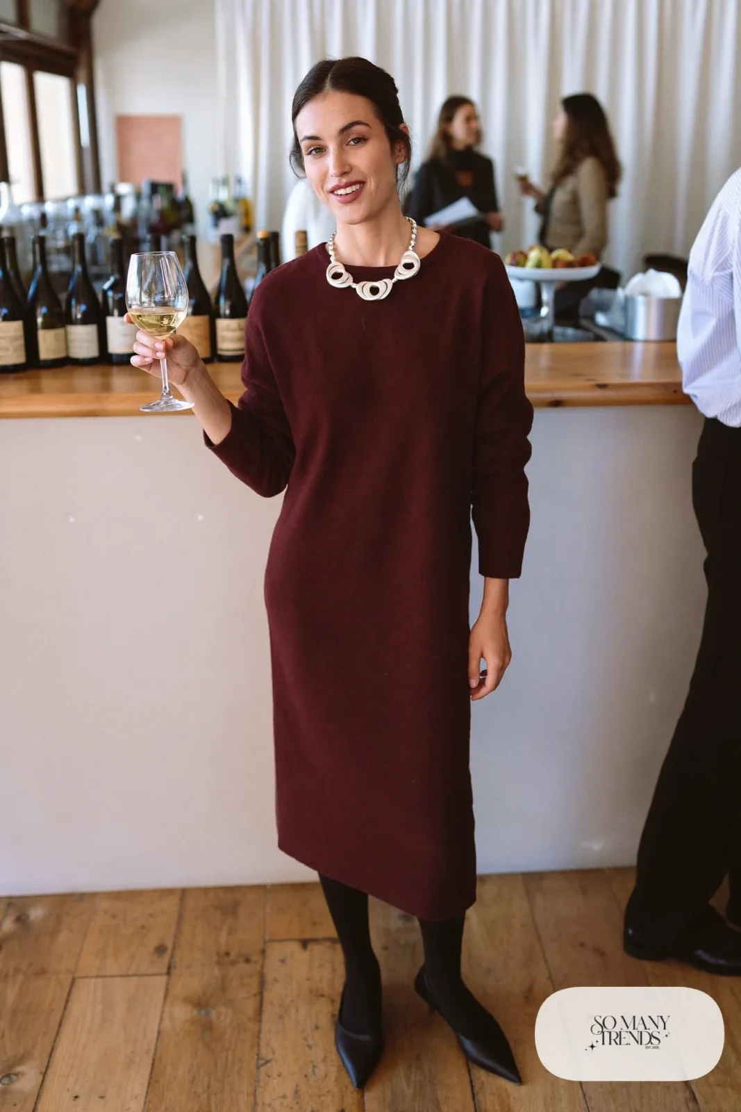 Woman in a relaxed wine knit midi dress with a chunky silver pendant necklace, black tights and pointed flats, outfit 20