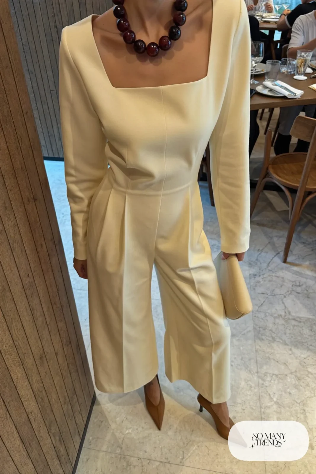 Woman in a cream wide-leg jumpsuit with wine statement beads and tan pumps, outfit 22