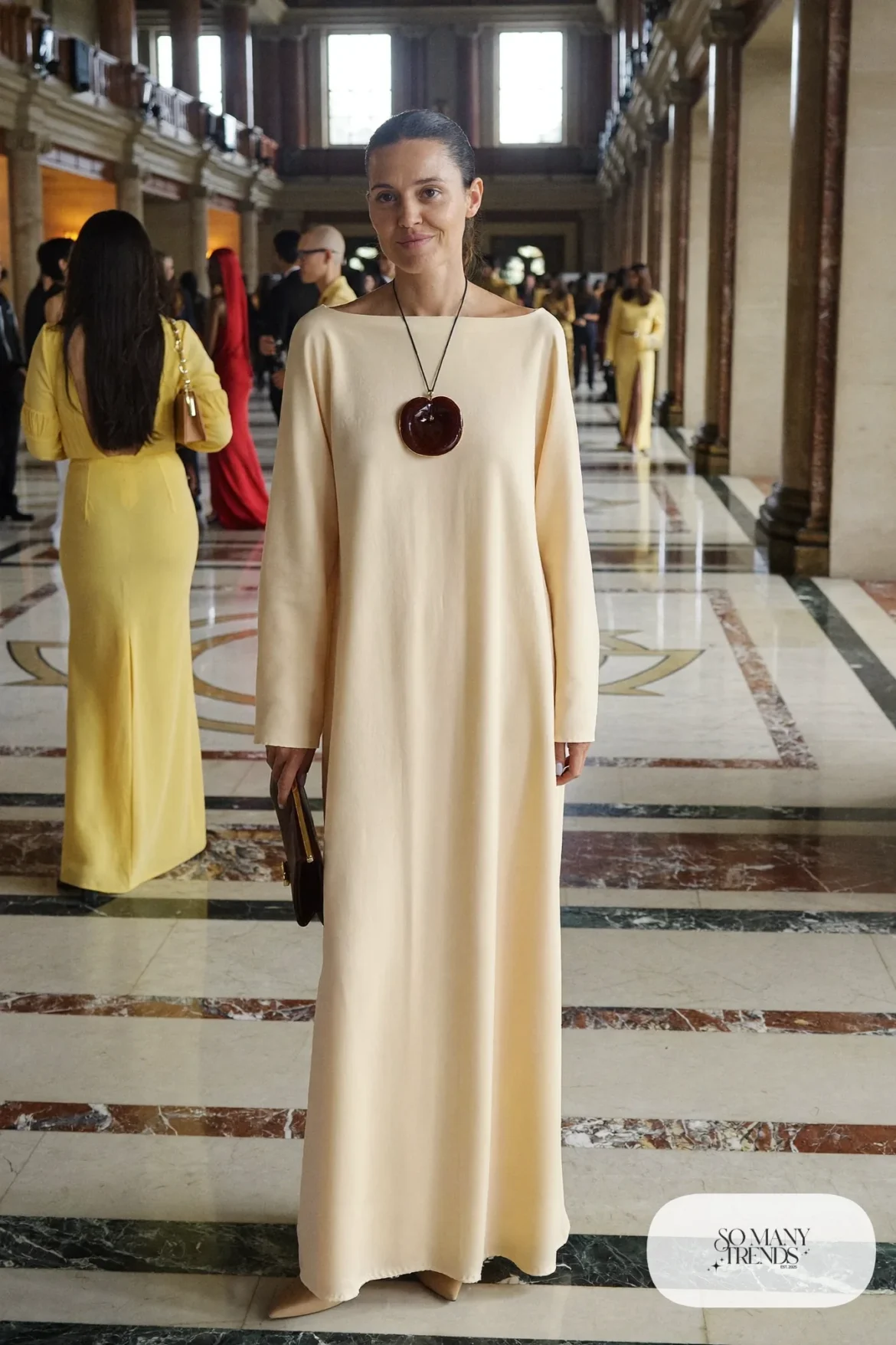 Woman in a cream floor-length boat neck column dress with a large wine pendant necklace and nude heels, outfit 26