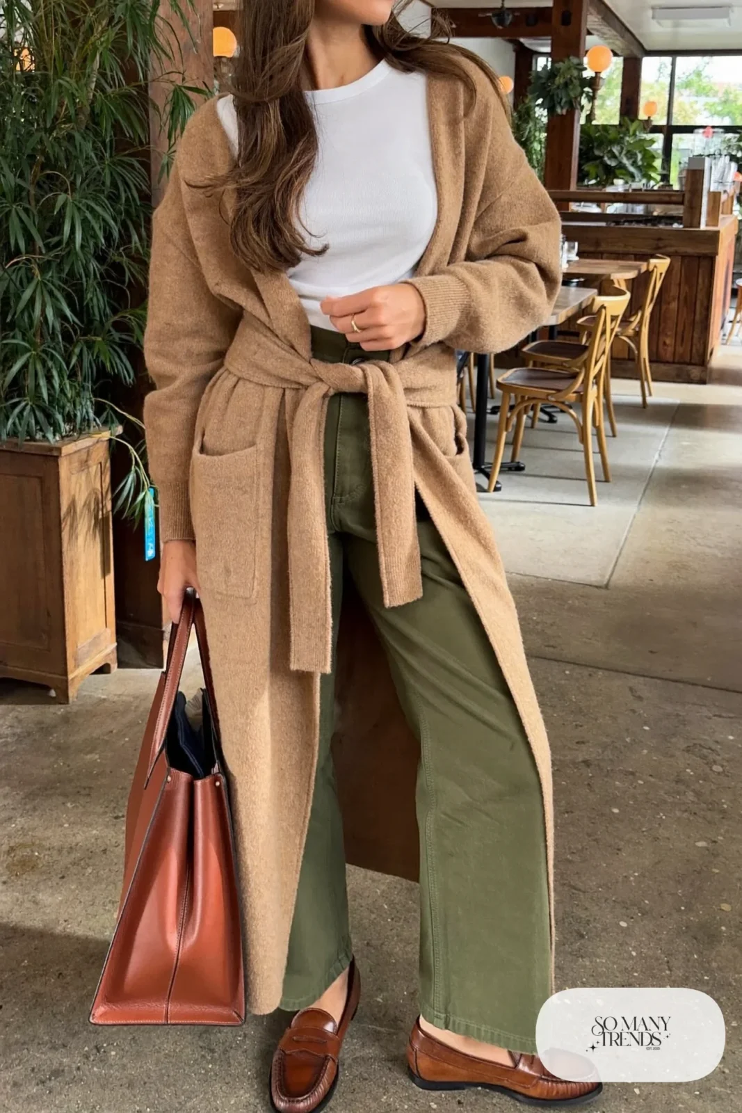 Woman in a long camel belted cardigan, white tee, olive pants and brown loafers, outfit 11