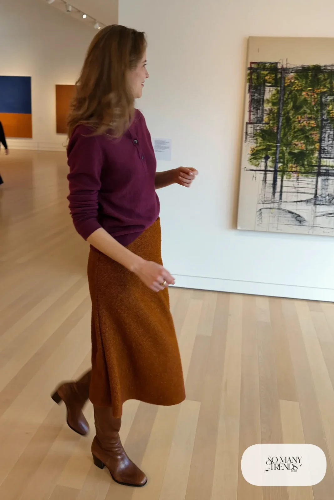 Woman in an eggplant sweater, rust midi skirt and brown tall boots at an art museum, outfit 16