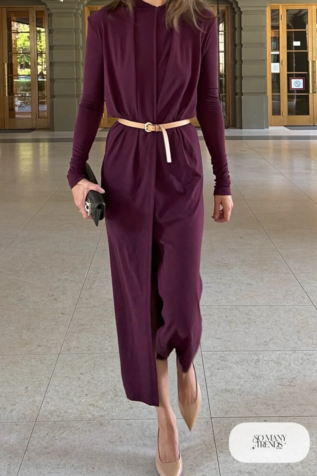 Woman in a draped plum jersey midi dress, camel belt and nude slingbacks at a theater lobby, outfit 23