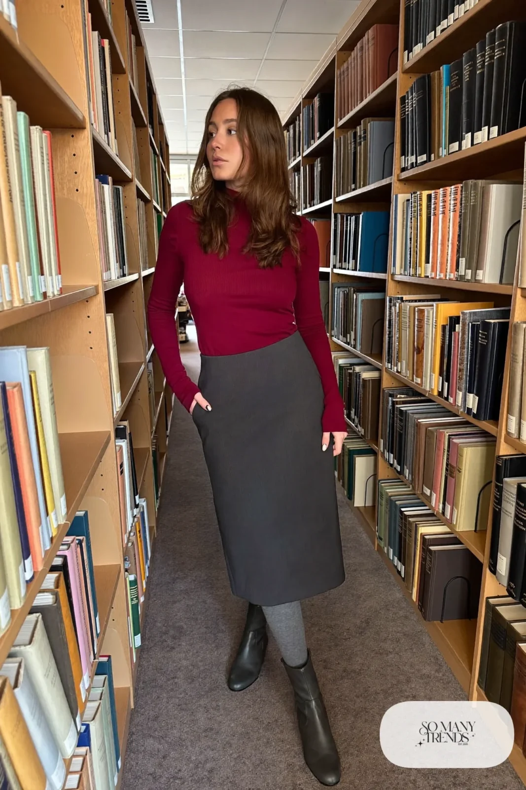 Woman in an eggplant turtleneck, gray midi skirt, gray tights and flat boots in a library, outfit 27