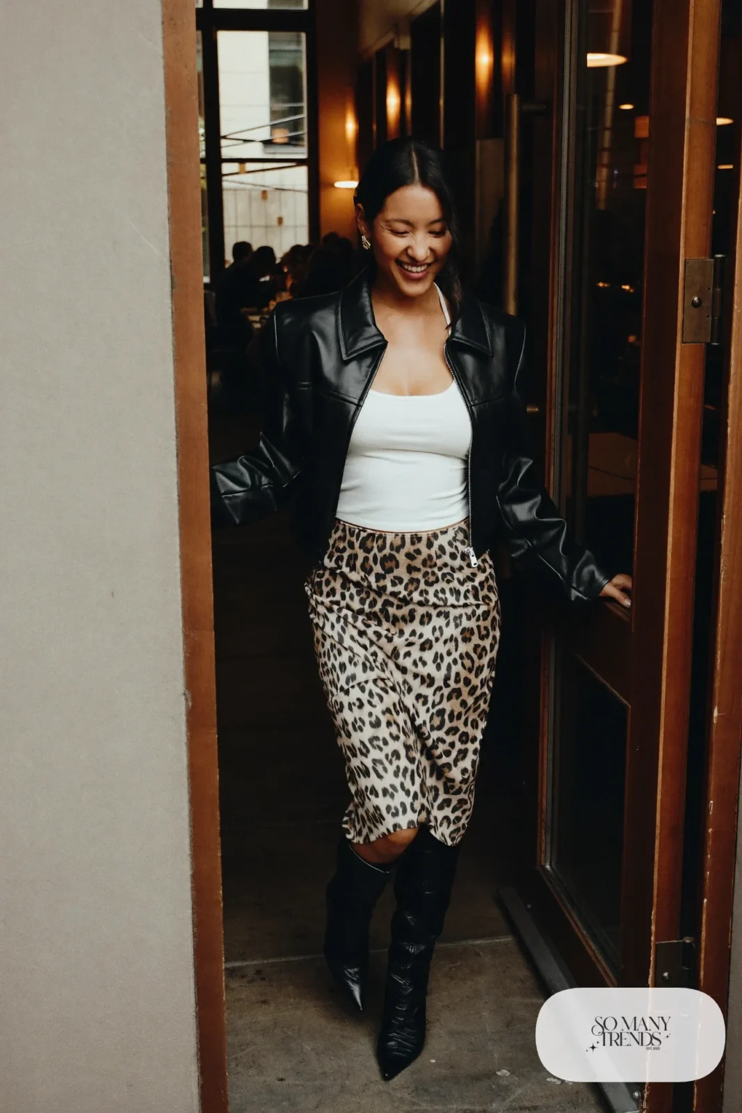Woman in a short black leather jacket over a white tank, leopard print midi skirt and black pointed boots, outfit 14