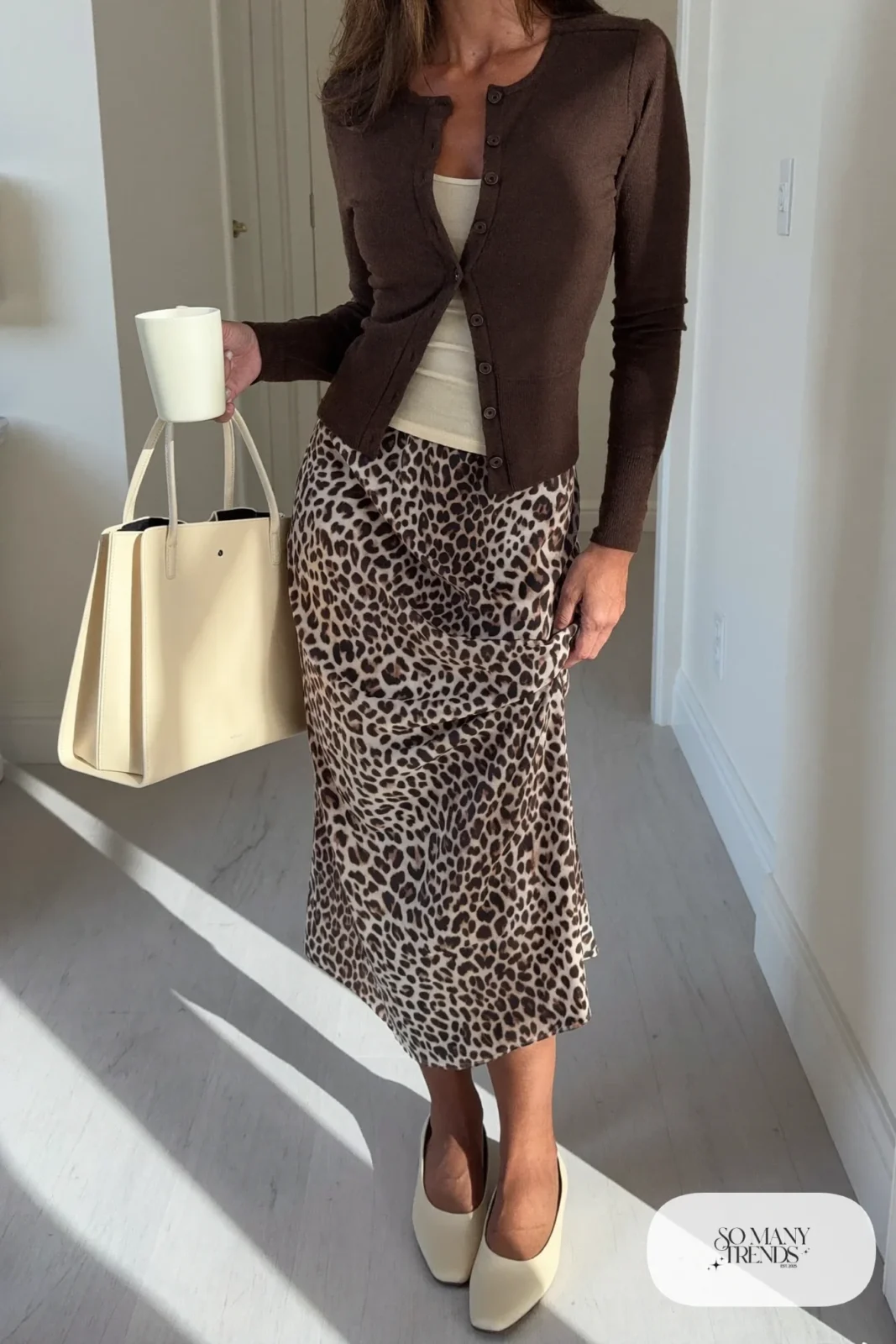 Woman in a chocolate brown buttoned cardigan over a tank, cheetah print midi skirt and ecru flat shoes, outfit 23