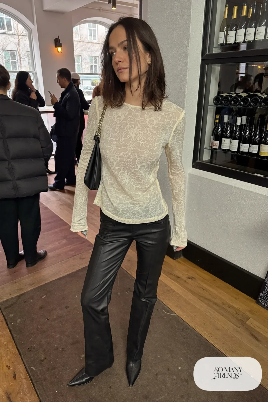Ivory long-sleeve lace top with black straight-leg faux leather pants, pointed ankle boots and a small black bag, look 11