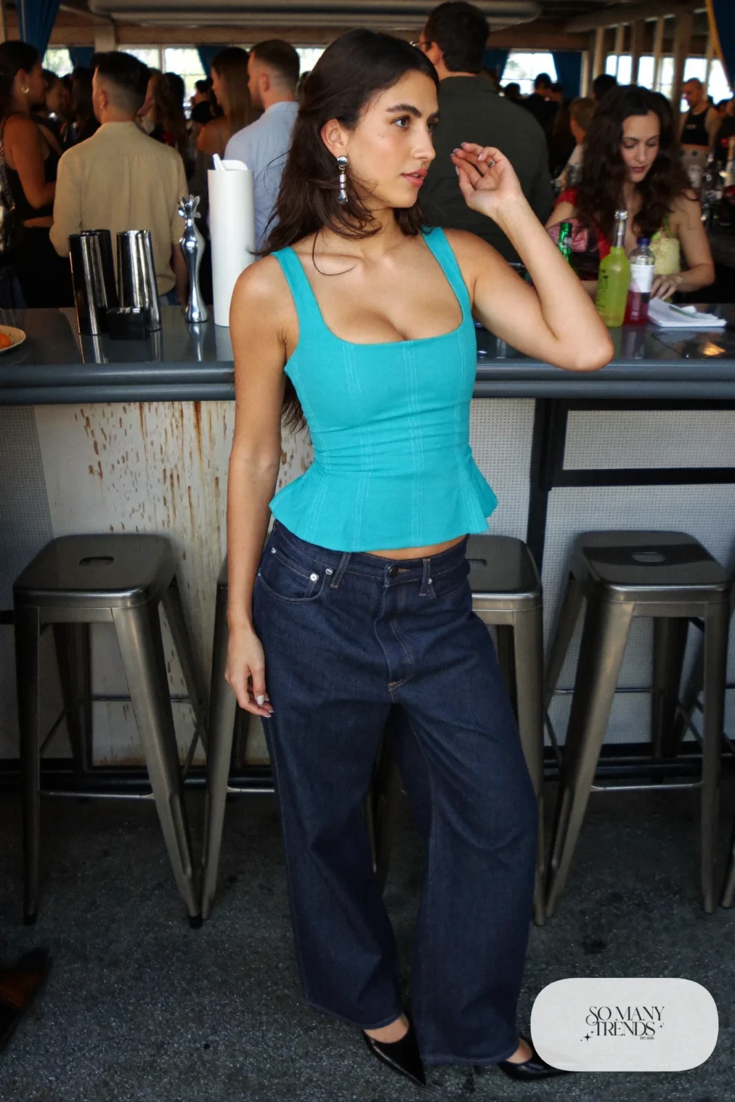 Woman in a turquoise corset-style top, dark wide jeans, silver earrings and pointed pumps, outfit 17
