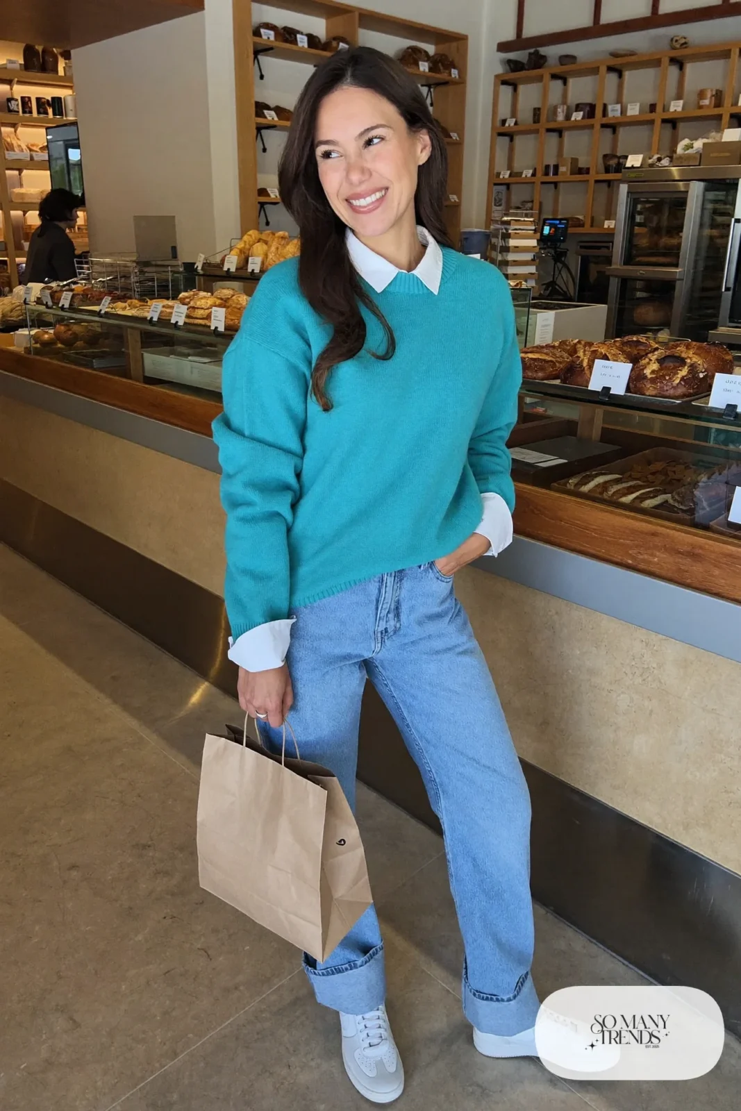 Woman in a turquoise crewneck sweater, white shirt collar, straight blue jeans and white sneakers, outfit 22