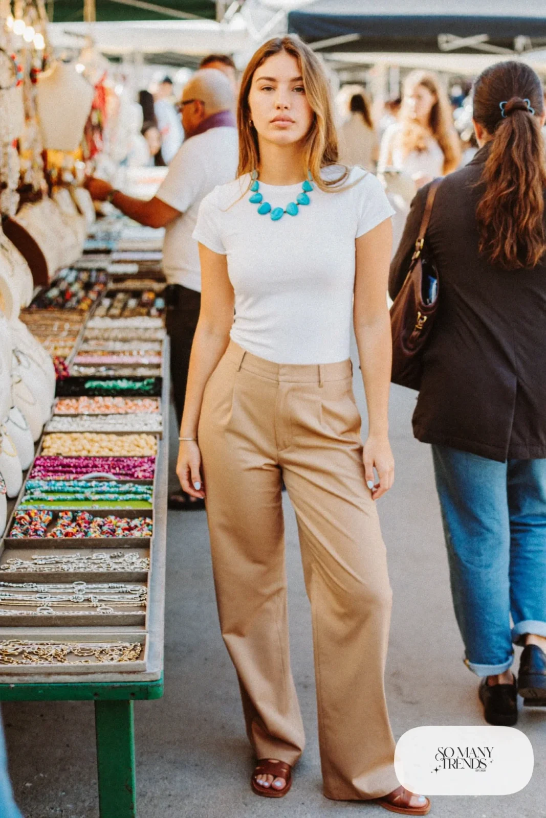 Woman in a white tee, a chunky turquoise stone necklace, tan pants and brown sandals, outfit 25