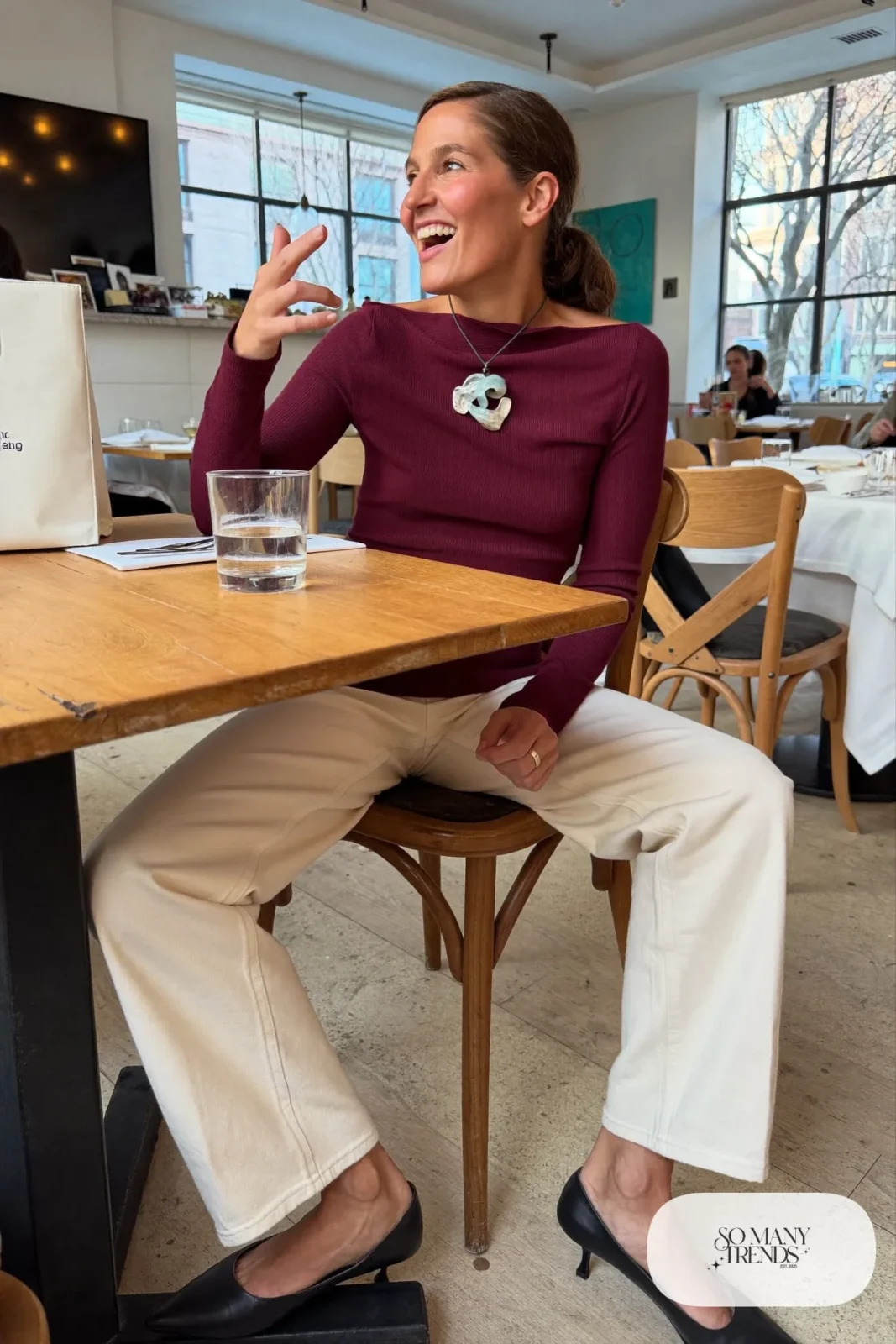 Woman in a wine boat neck sweater with a large pendant necklace, cream straight pants and pointed flats, outfit 2