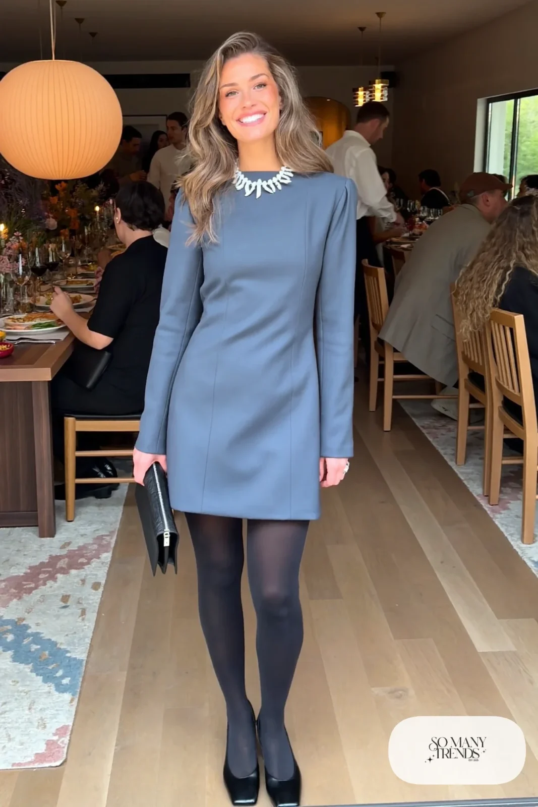 Woman in a slate blue structured mini dress with a bold crystal strand necklace, black tights and block heels, outfit 25