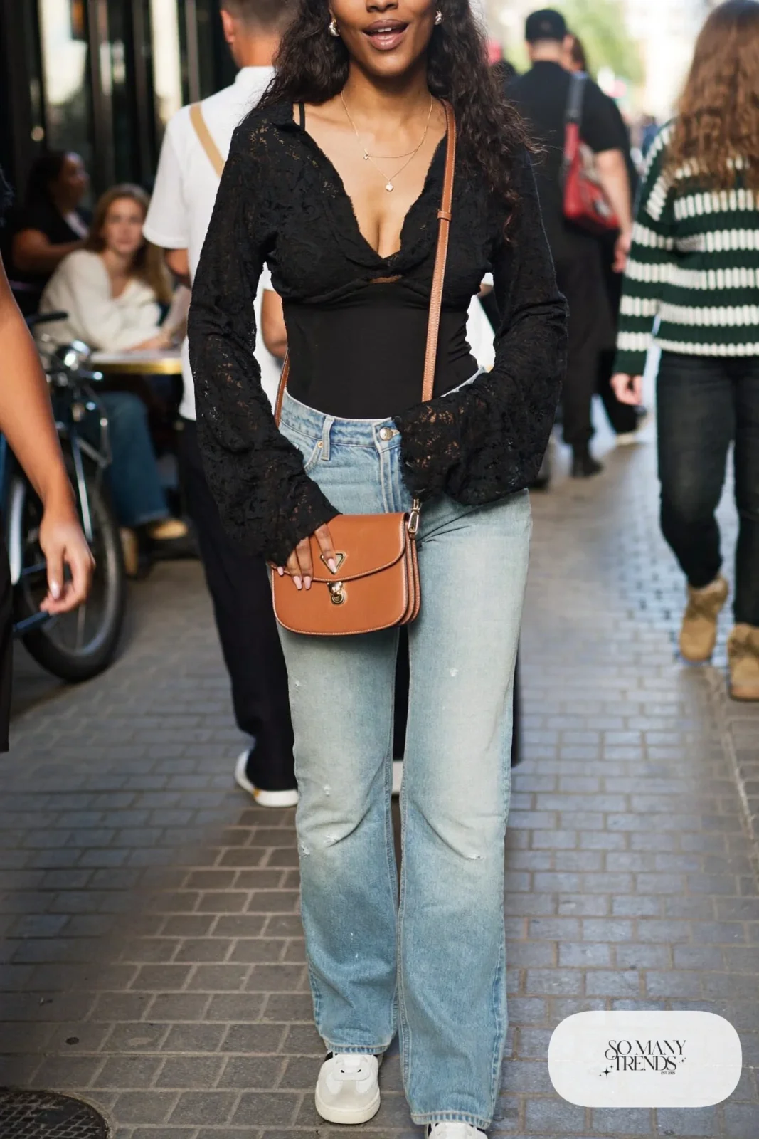 Black long-sleeve lace top with light wash straight-leg jeans, white leather sneakers and a small tan bag, look 1