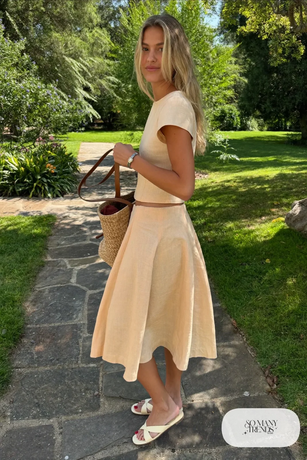 Woman in a peach linen matching skirt and top set with cream sandals and a straw bag, garden party outfit 13