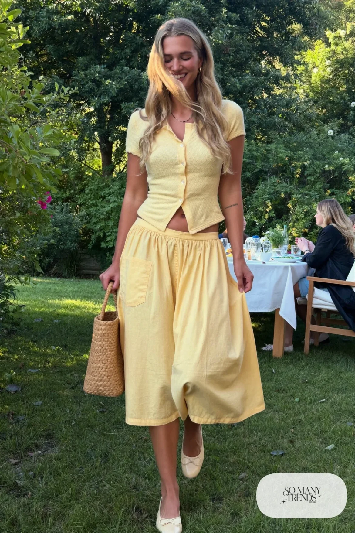 Woman in a butter yellow cotton knit top and pleated midi skirt set with cream bow flats, garden party outfit 15
