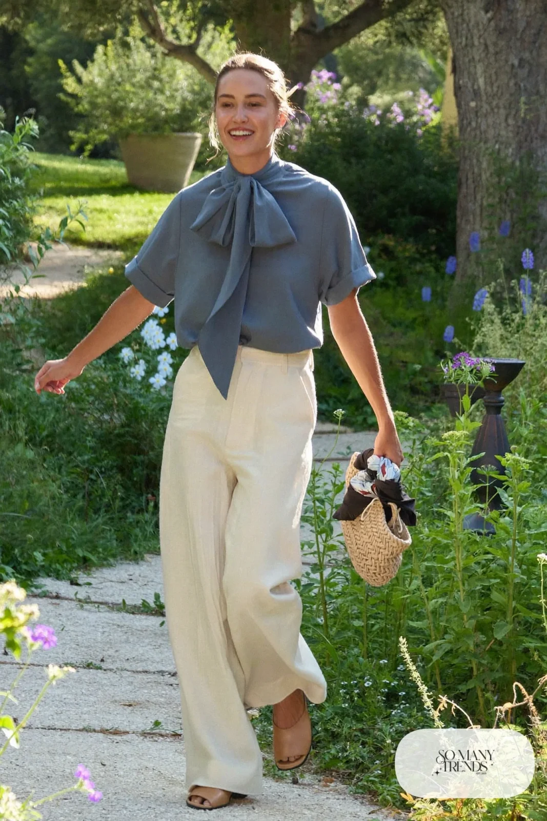 Woman in a slate blue matte blouse and cream wide-leg linen pants with flat mules, garden party outfit 20