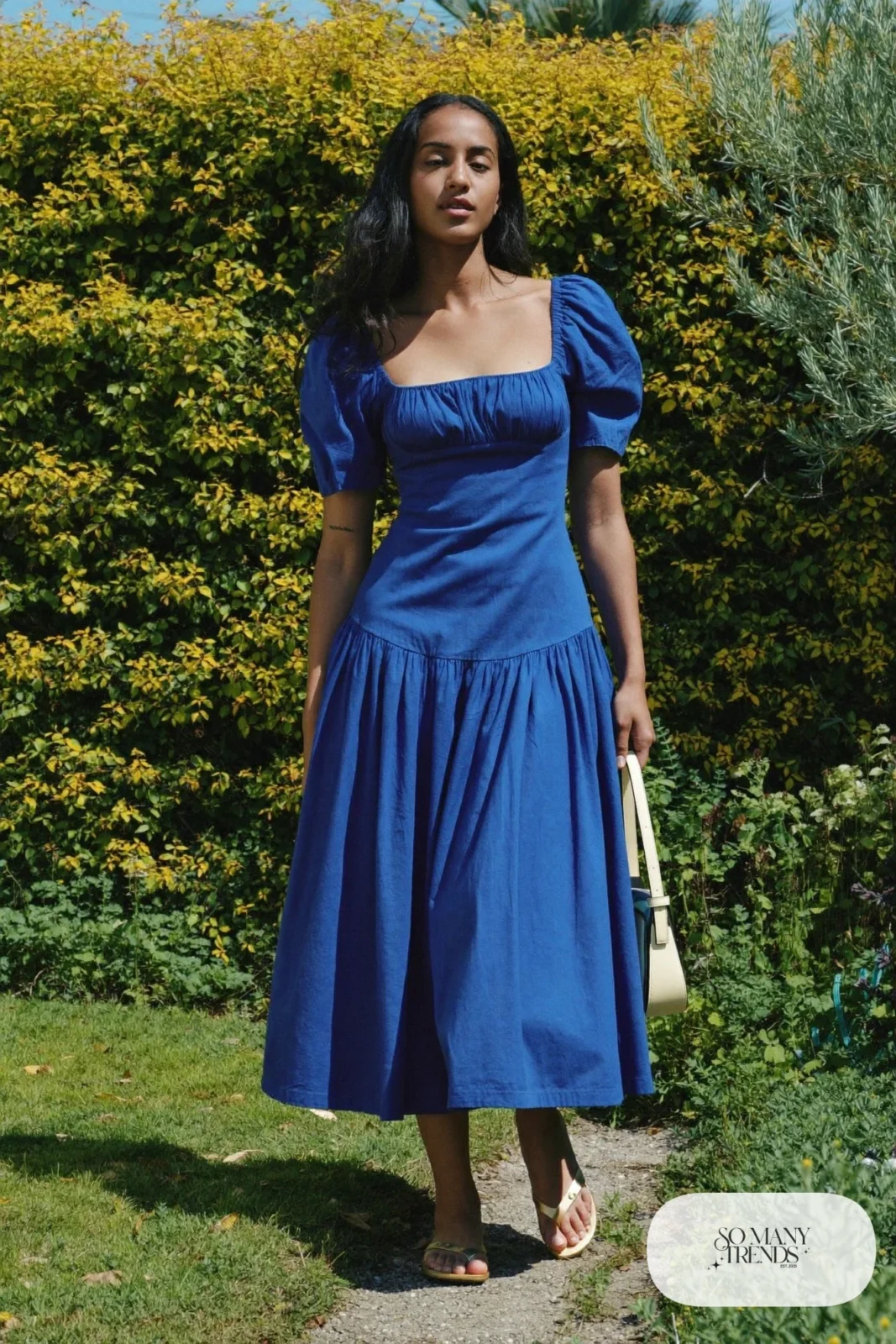 Woman in a cobalt blue cotton poplin midi dress with gold flat sandals and a small bag, garden party outfit 26