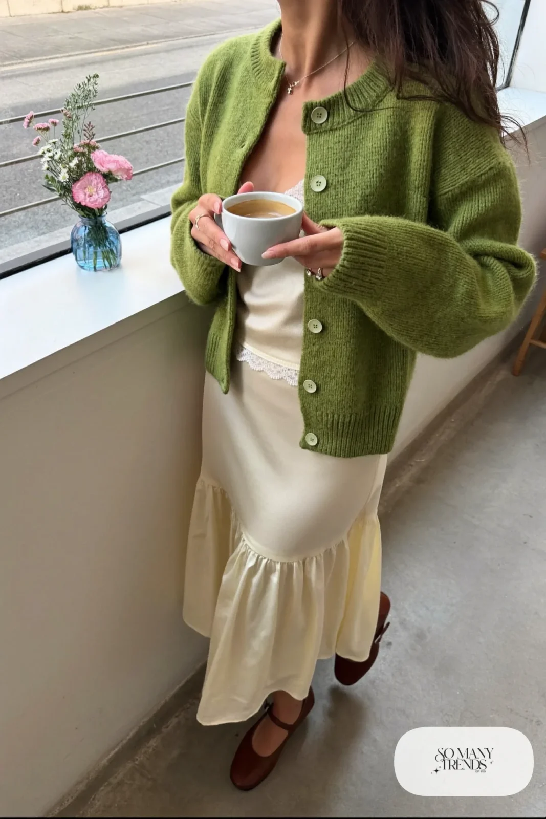Woman in a moss green knit cardigan, cream cami, cream flowy midi skirt and cognac mary janes at a brunch cafe, look 5