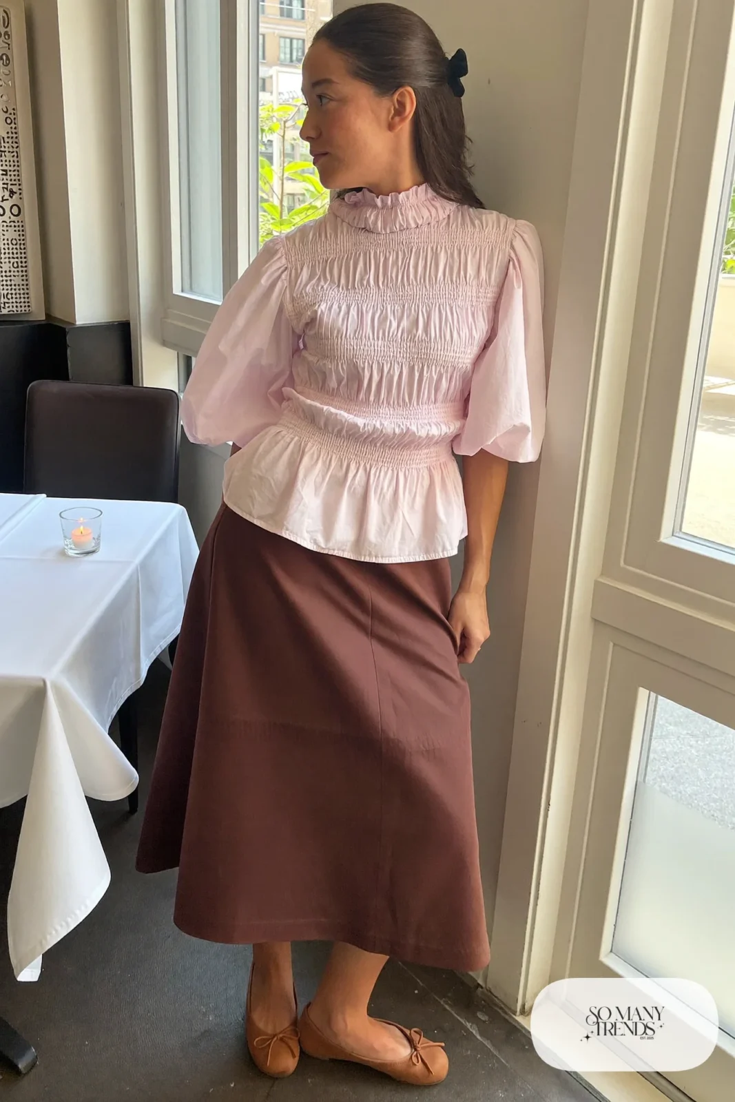 Woman in a pink puff sleeve blouse, chocolate brown midi skirt and cognac flats in a restaurant, look 7