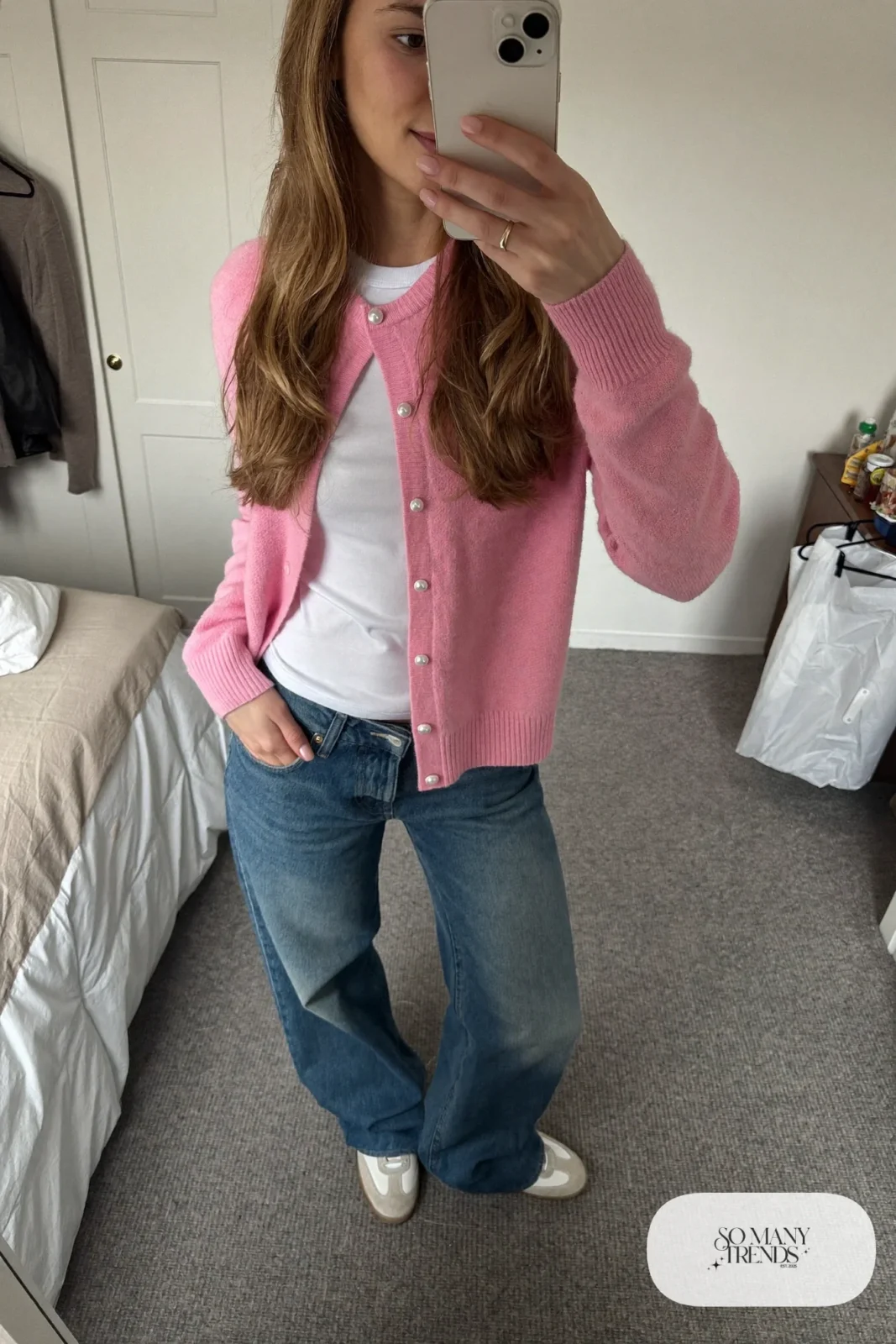 Woman in a pink knit cardigan with pearl buttons, white tee, blue straight jeans and white sneakers at a bakery, look 8