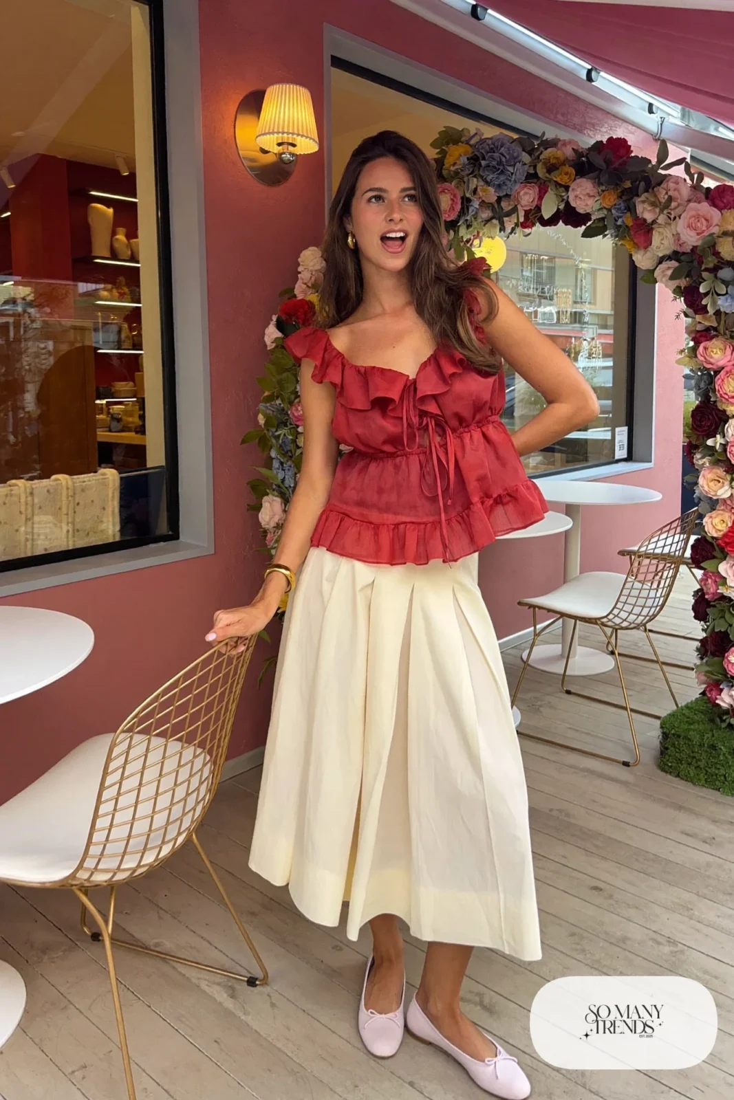 Woman in a red ruffle top, cream pleated midi skirt and pink ballet flats at a pink brunch spot, look 9