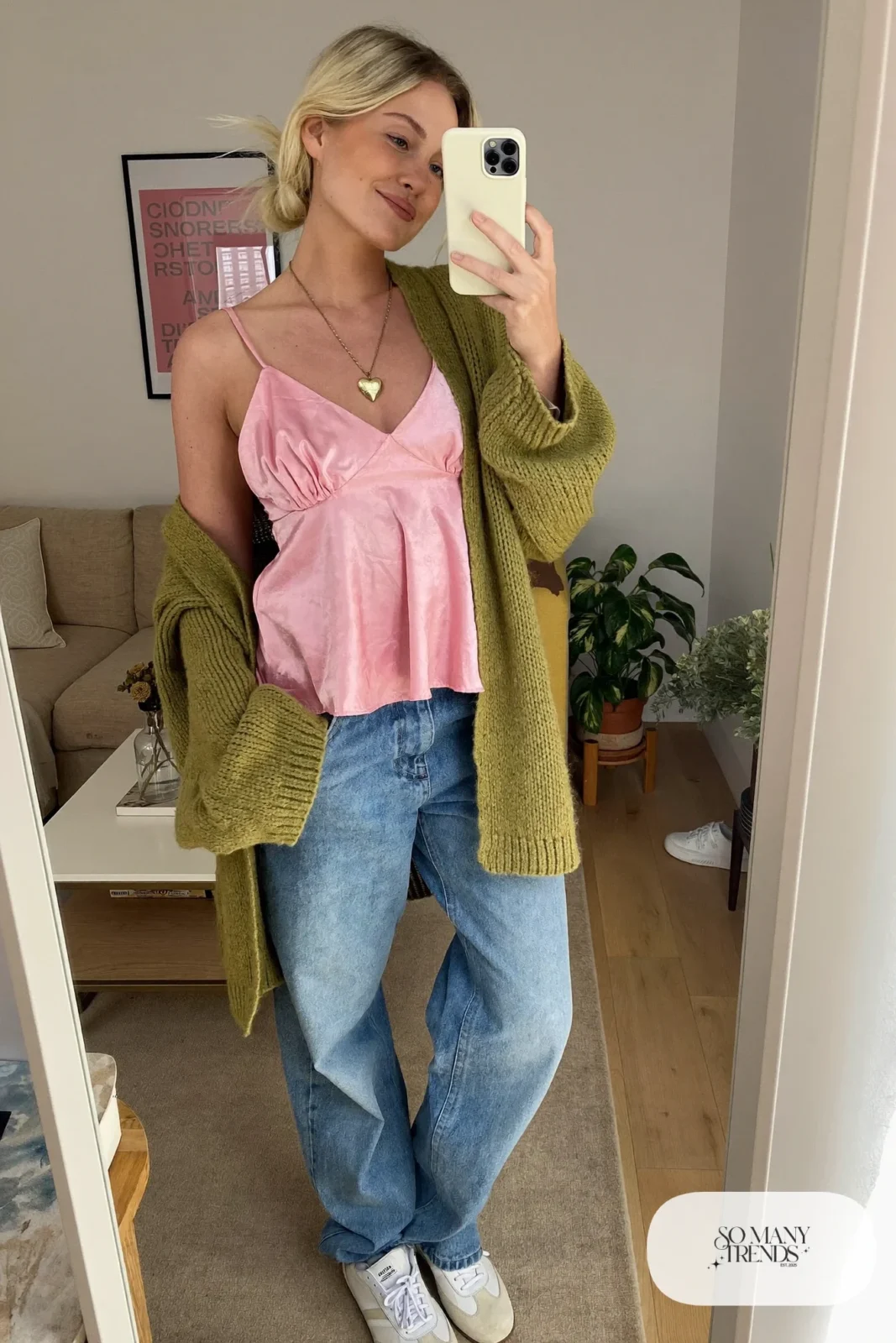 Woman in a pink satin cami, moss green cardigan, light jeans and white sneakers at a cafe table, look 12