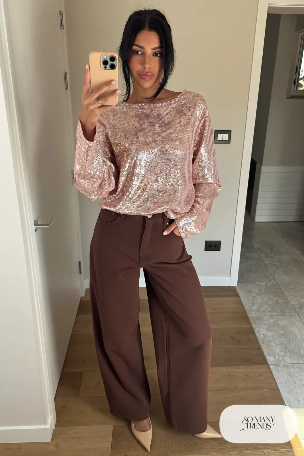 Woman in a pink sequin top, chocolate brown wide-leg pants and heels at a restaurant, look 20