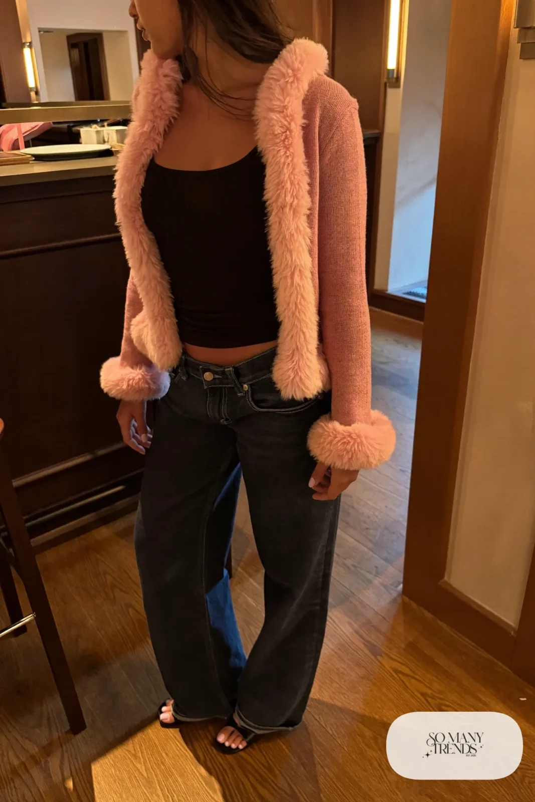 Woman in a pink marabou trim cardigan, black tank, dark straight jeans and heels at a restaurant bar, look 21