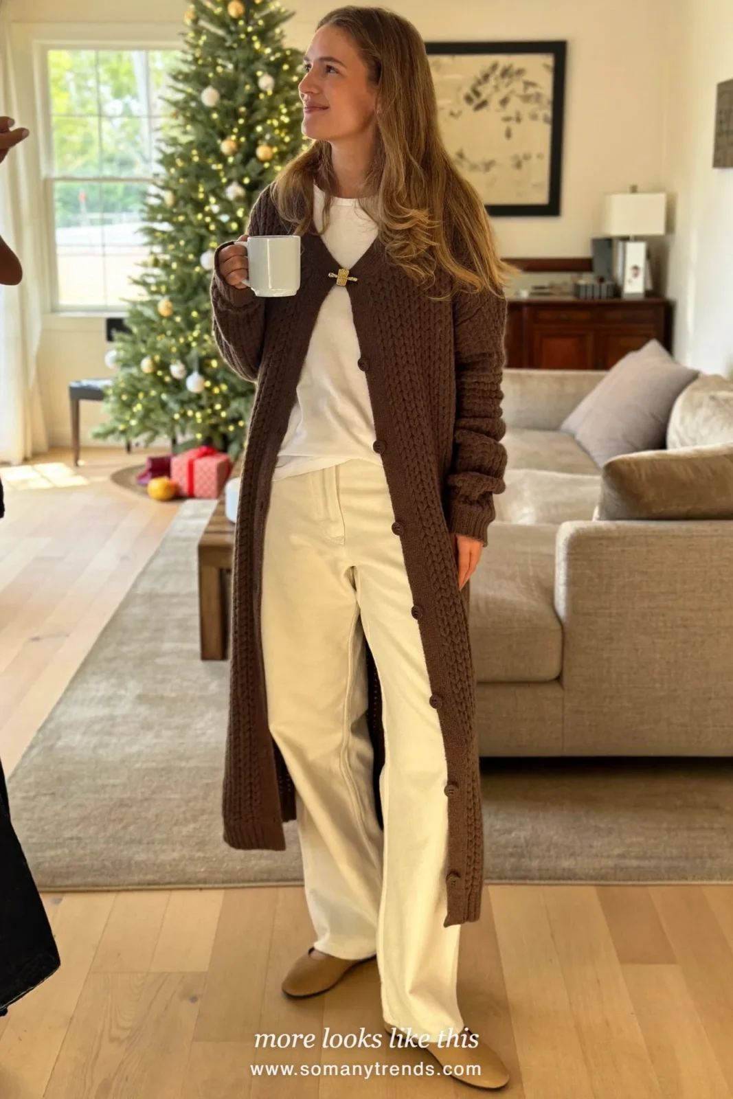 Long chocolate cardigan with a brooch over a white tee and straight ecru pants, Christmas outfit 17