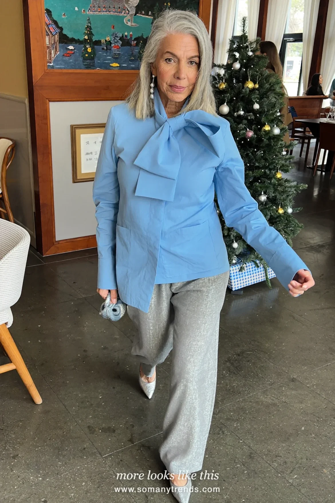 Woman in an icy blue poplin bow blouse, light gray straight pants and silver pointed flats at an early Christmas dinner, outfit 23