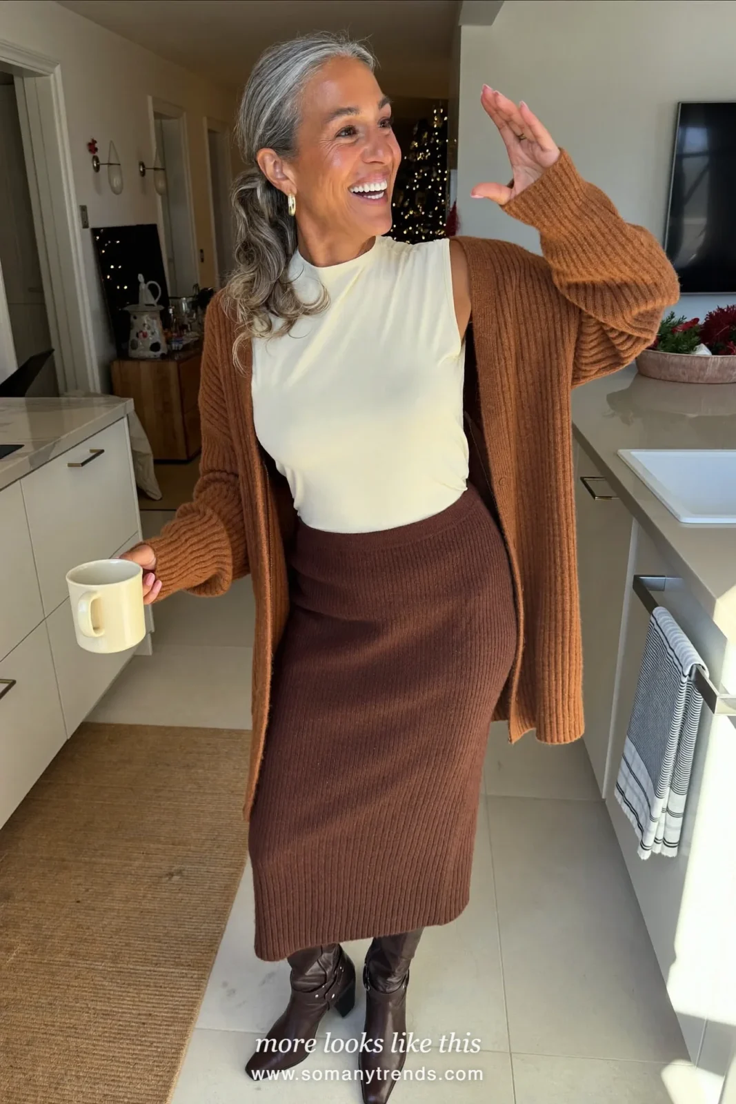 Woman in a chocolate brown knit cardigan, cream shell, brown ribbed midi skirt and brown boots on Christmas morning, outfit 26