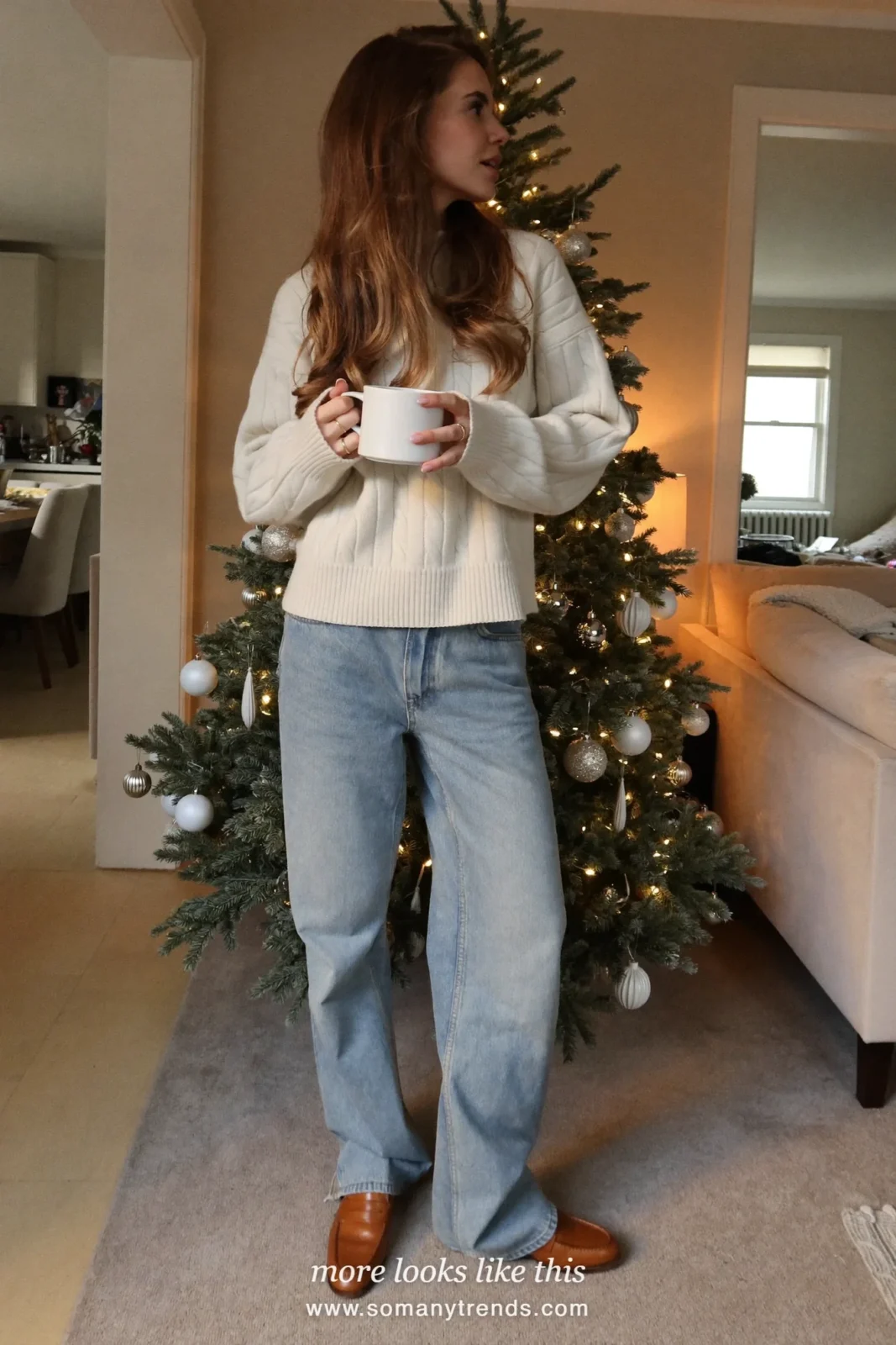 Woman in a cream cable knit sweater, relaxed blue jeans and brown penny loafers in a living room, outfit 1