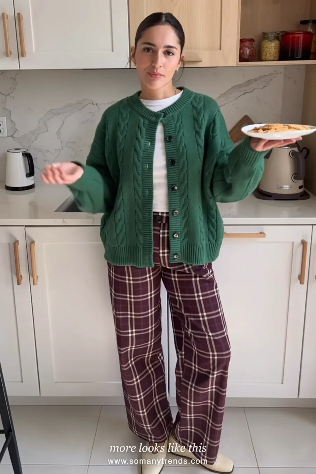 Woman in a forest green cable cardigan, white tee, burgundy plaid wide-leg pants and cream flats in a kitchen, outfit 6