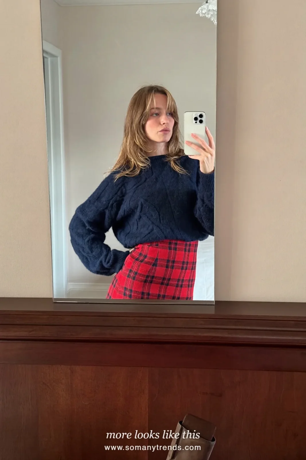 Woman in a navy cable sweater, red plaid midi skirt and brown boots in a dining room, outfit 8