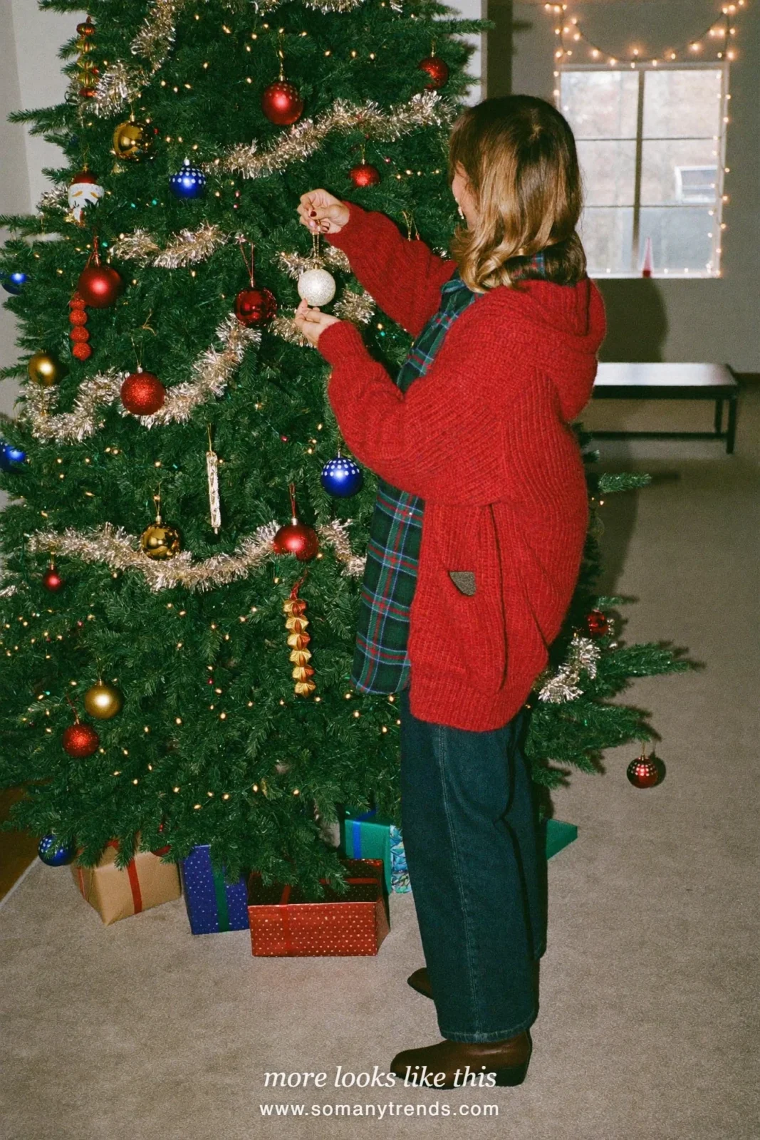 Woman in a plaid flannel shirt, deep red cardigan, dark jeans and boots decorating a tree, outfit 23