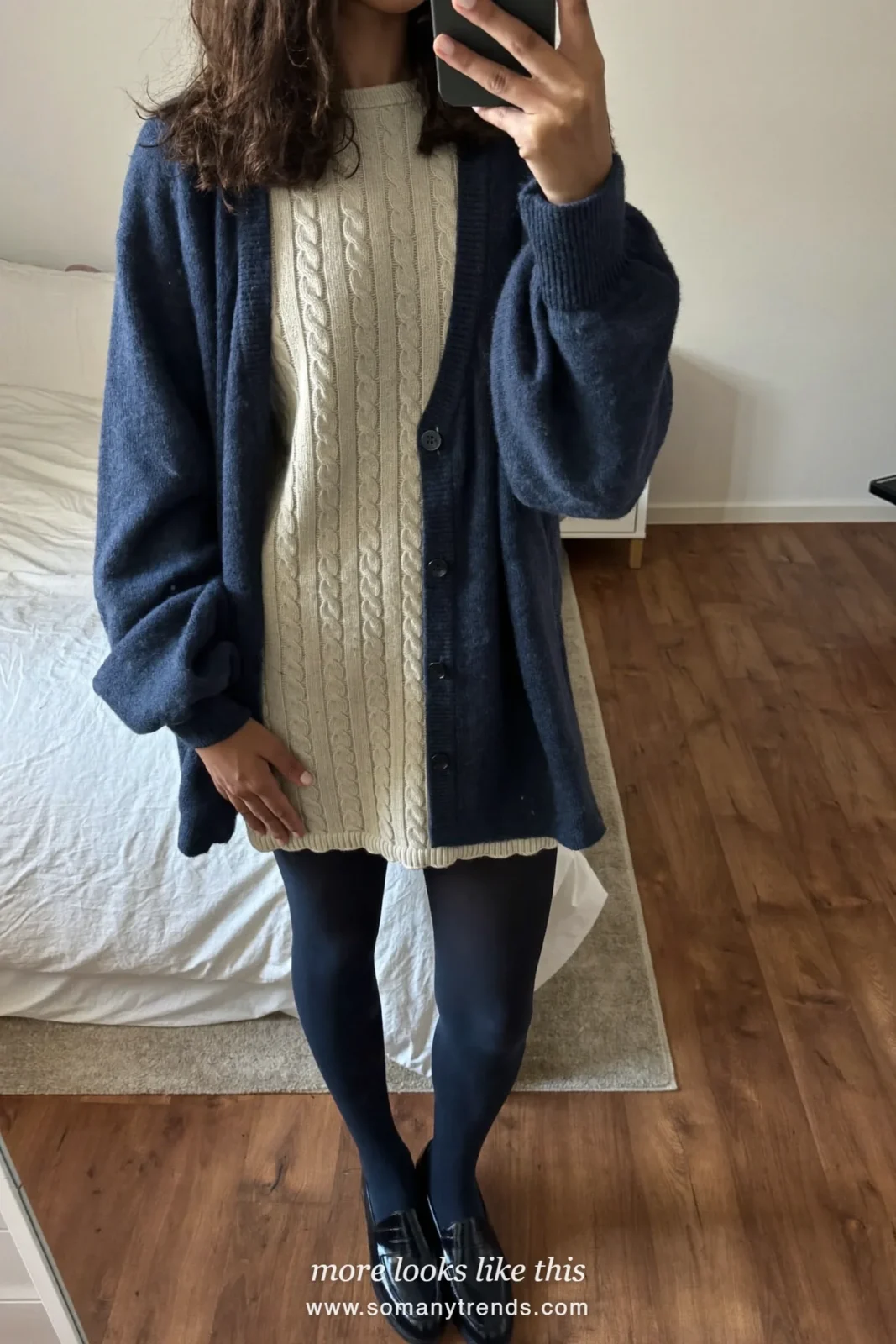 Woman in an ivory cable knit mini dress, navy cardigan, navy tights and loafers in a living room, outfit 28