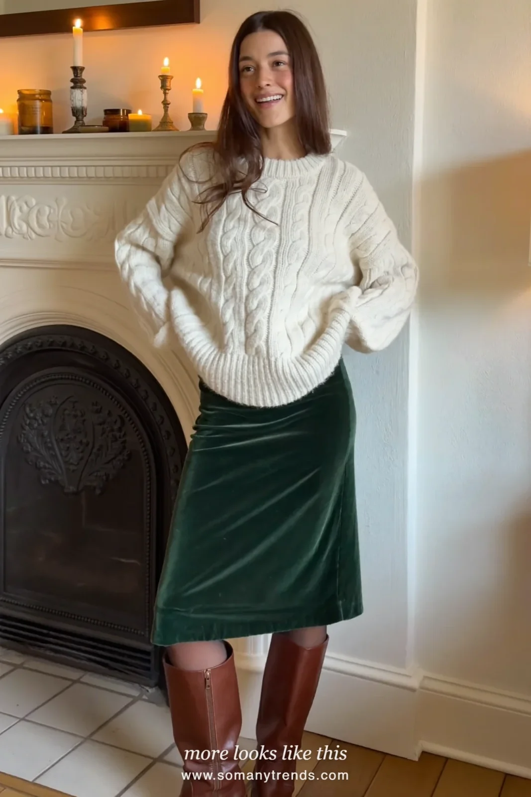Woman in a forest green velvet midi skirt, cream cable knit and brown boots near a fireplace, outfit 29