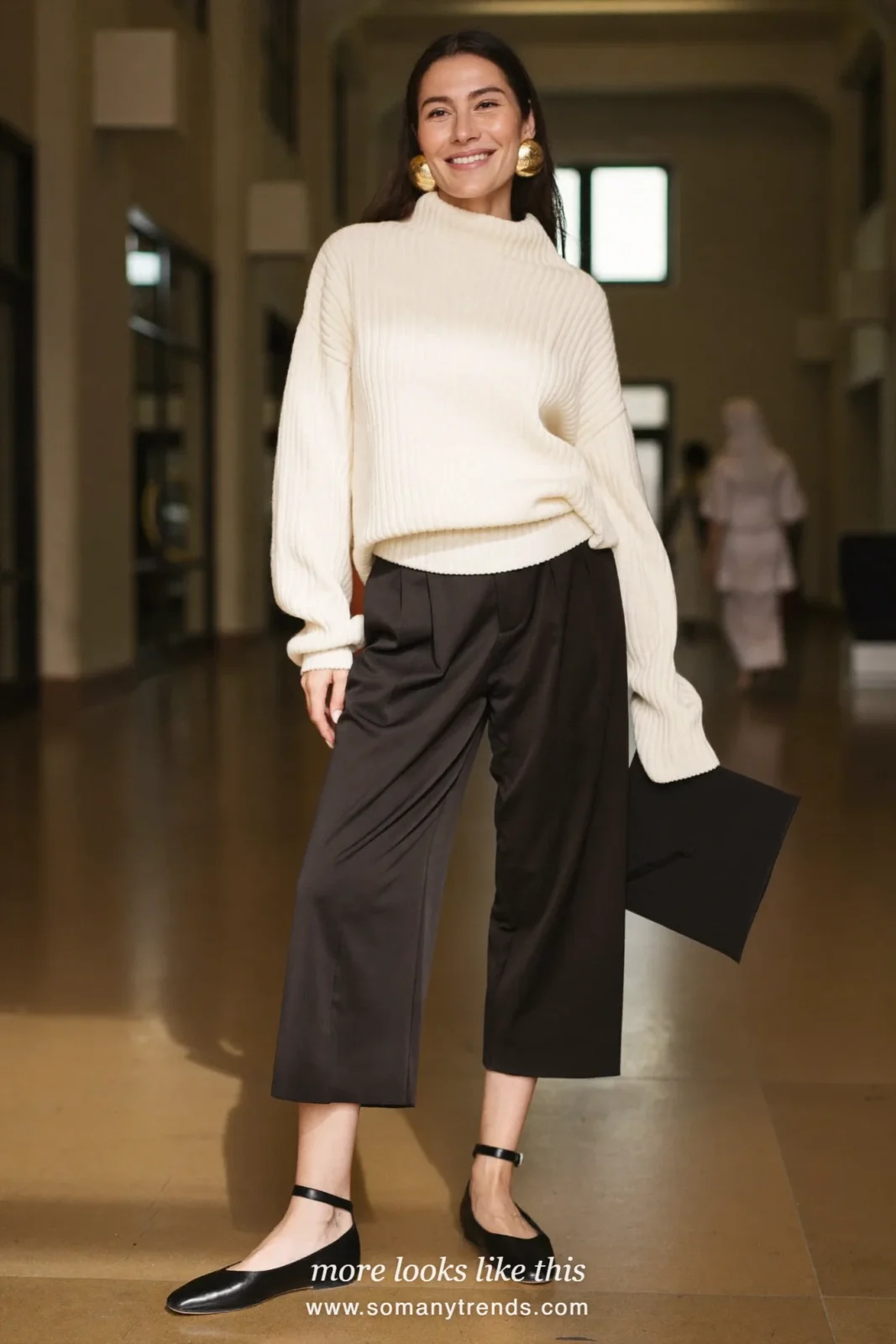 Woman wearing an ivory ribbed mock-neck sweater, wide-leg black pants, large gold statement earrings and black ankle-strap flats, winter graduation outfit 9