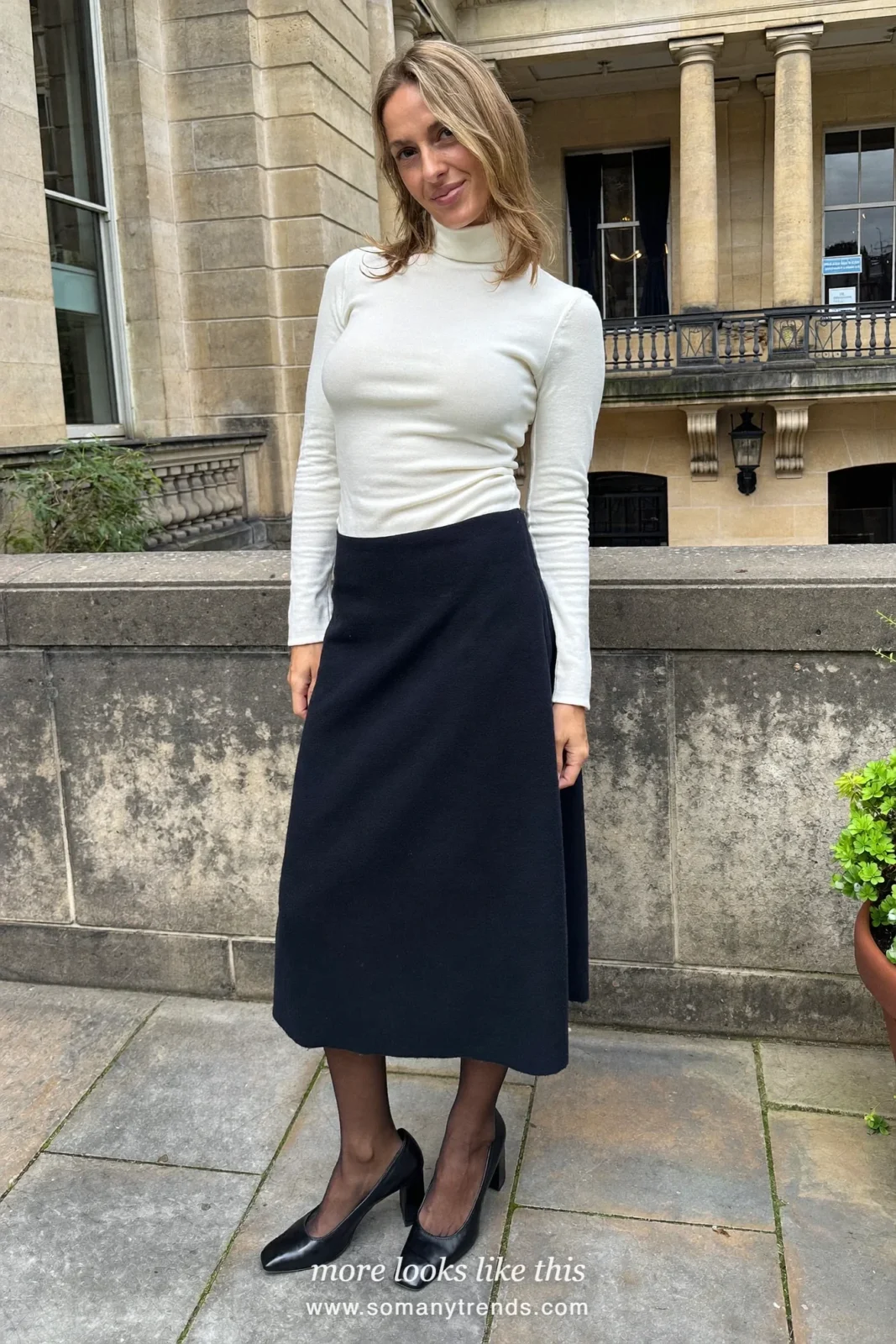 Woman wearing an ivory fitted turtleneck, navy wool A-line midi skirt, sheer black tights and black block-heel pumps, winter graduation outfit 13