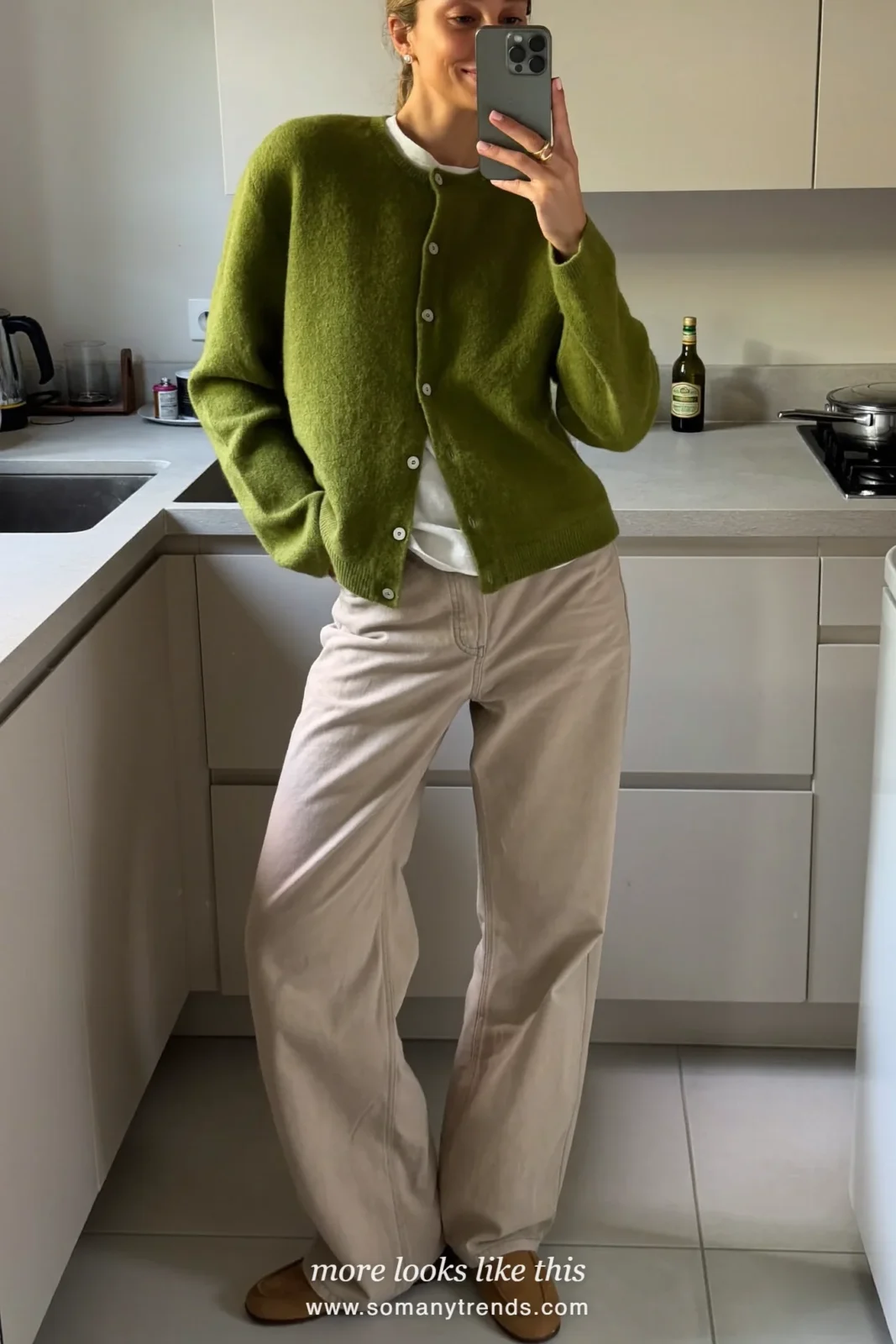 Woman wearing a pine green button cardigan over a white tee, wide-leg oatmeal pants and tan suede loafers, winter graduation outfit 20