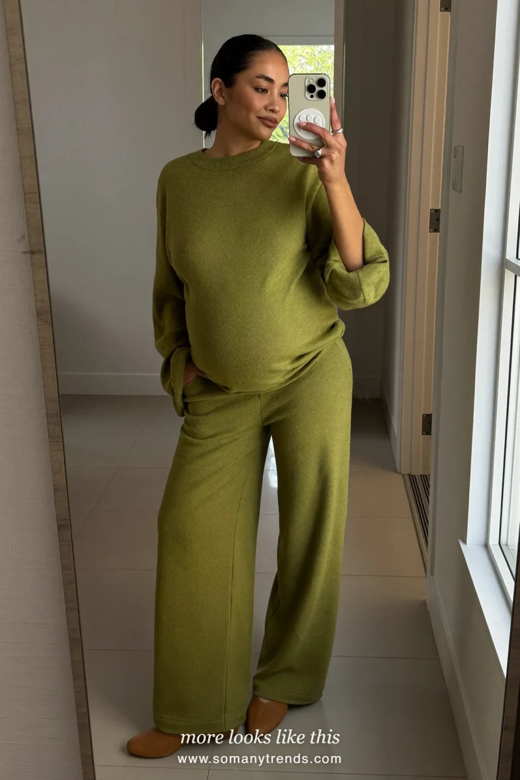 Woman with a baby bump taking a mirror selfie in a hallway in an olive knit tee, olive relaxed maternity pants and flats, outfit 4