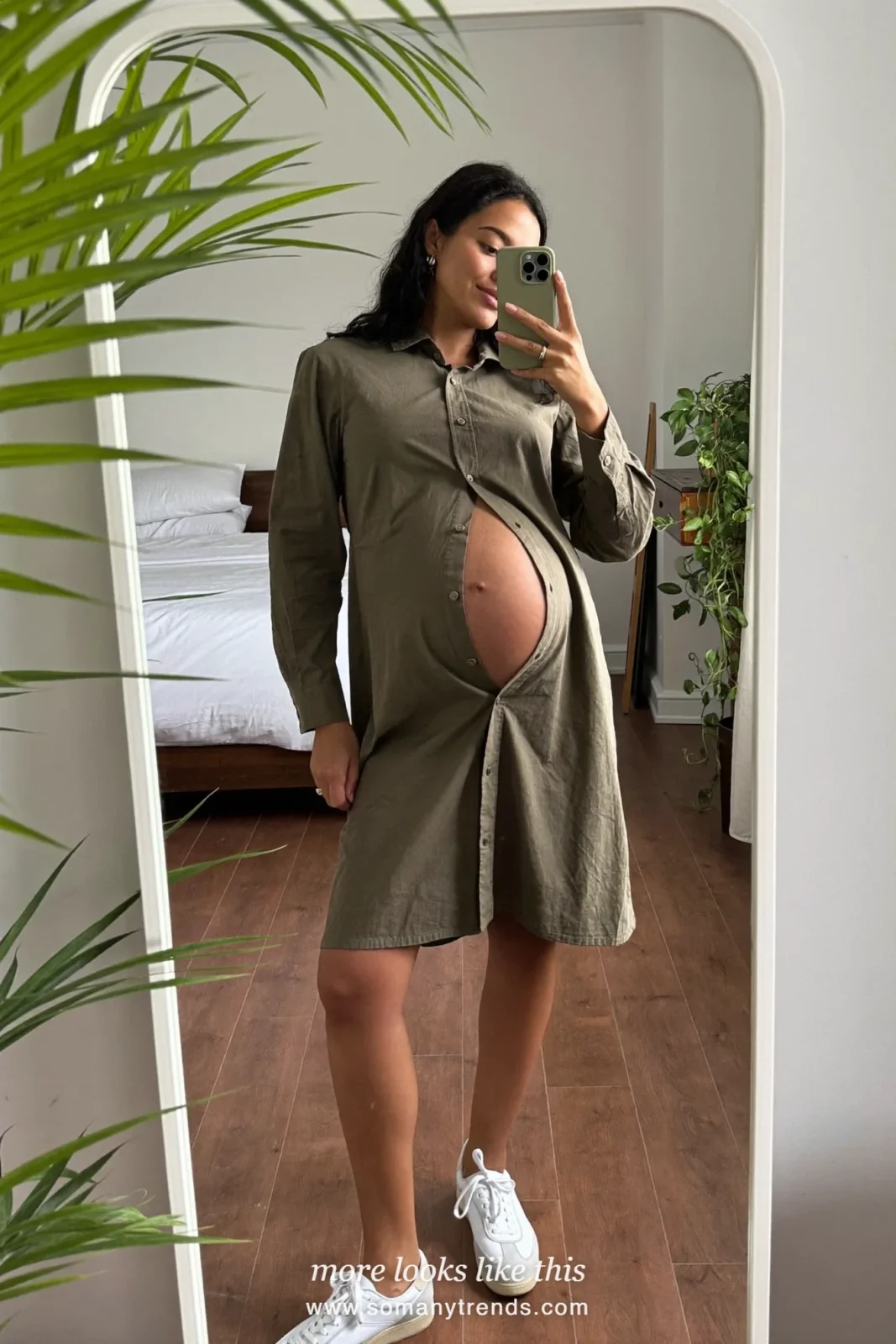 Woman with a baby bump taking a mirror selfie in a bedroom in an olive midi shirt dress and white sneakers, outfit 8