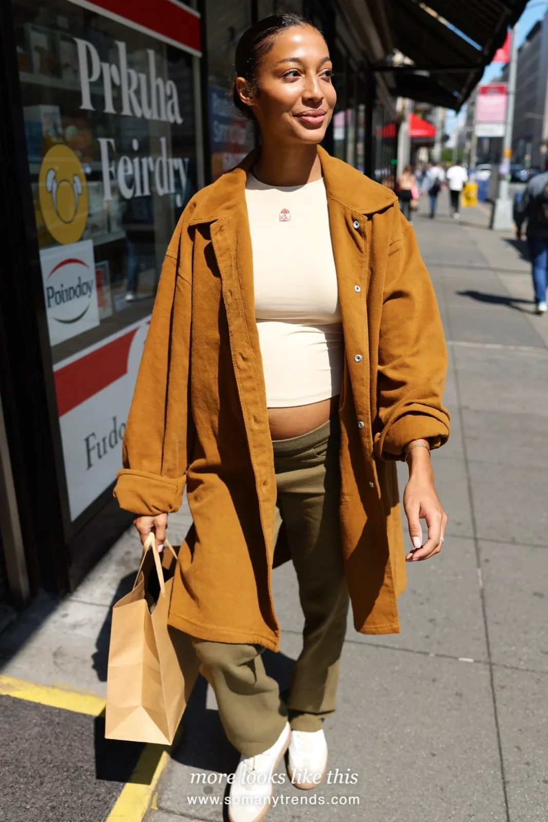 Woman with a baby bump in a long caramel overshirt open over an ivory tee, olive jersey maternity pants and sneakers, outfit 21