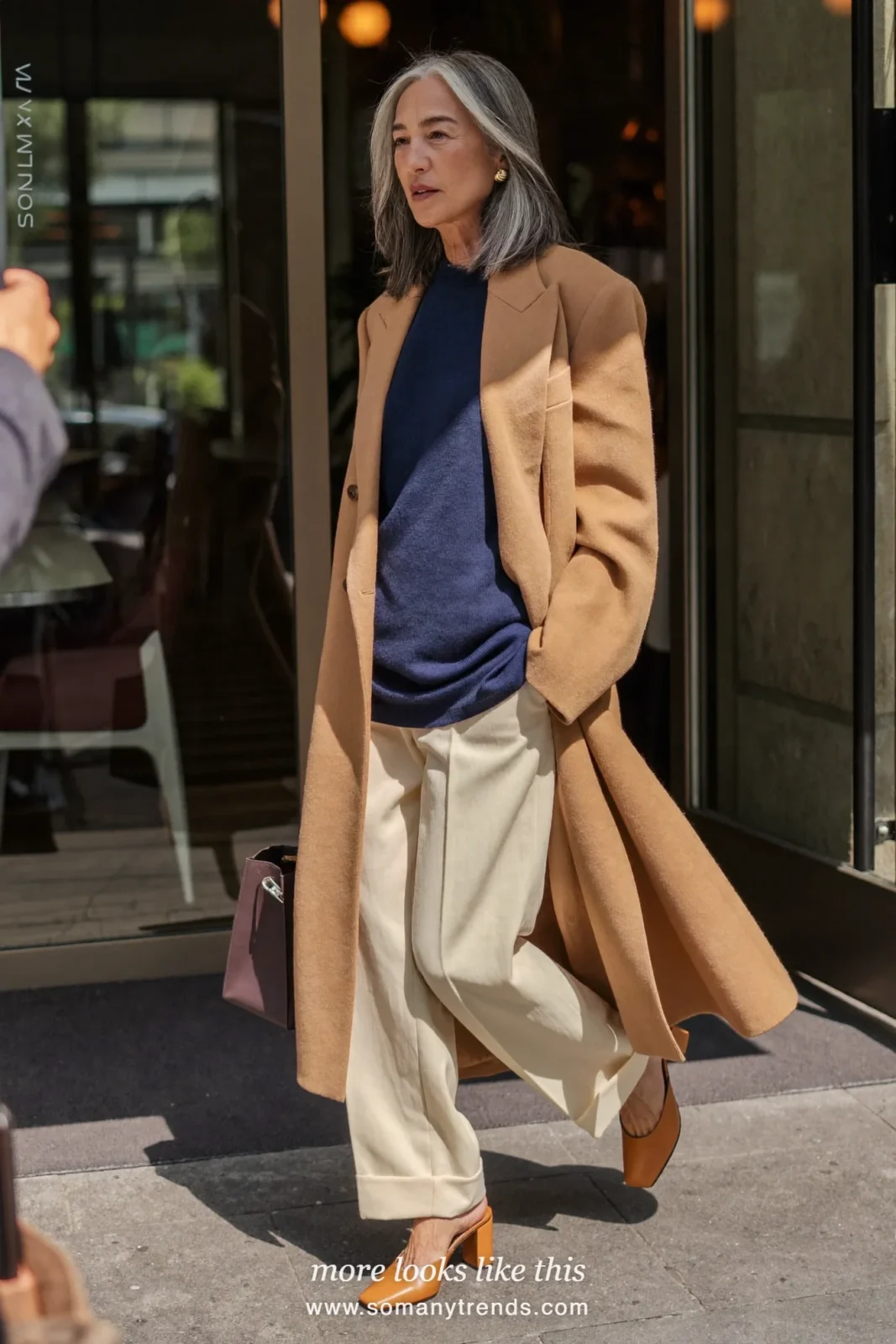 Woman in her forties wearing long camel blazer, fine indigo knit top, cream straight pants and tan block-heel mules, outfit 11