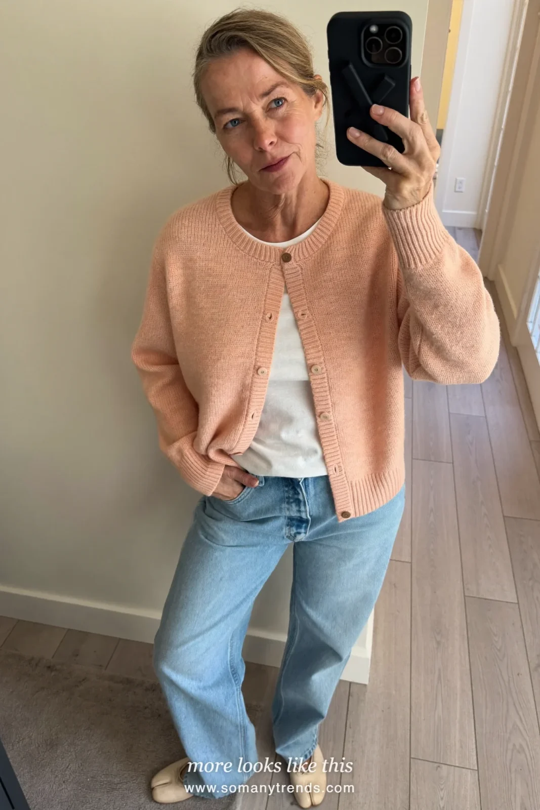 Woman over 50 in a peach cardigan over a white tee, straight blue jeans and ballet flats, mirror selfie at home, outfit 4